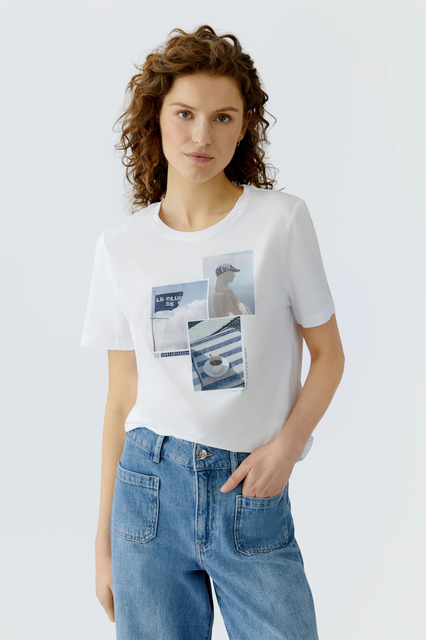Damen-T-Shirt: Junge Frau trägt ein weißes T-Shirt mit buntem Print und lässigen Jeans.