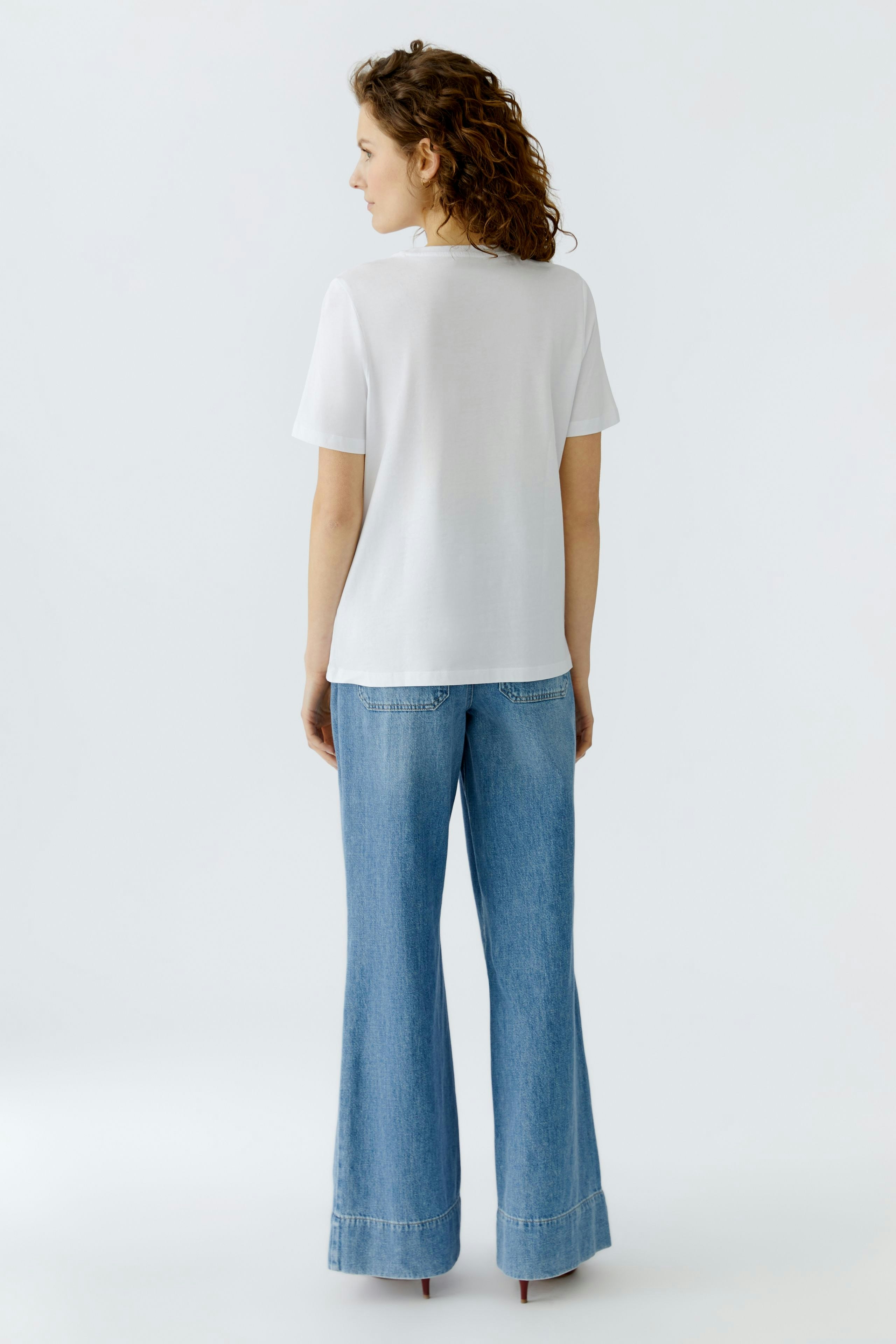 Casual women's T-shirt: A woman in a white T-shirt and wide-leg jeans stands with her back to the camera.