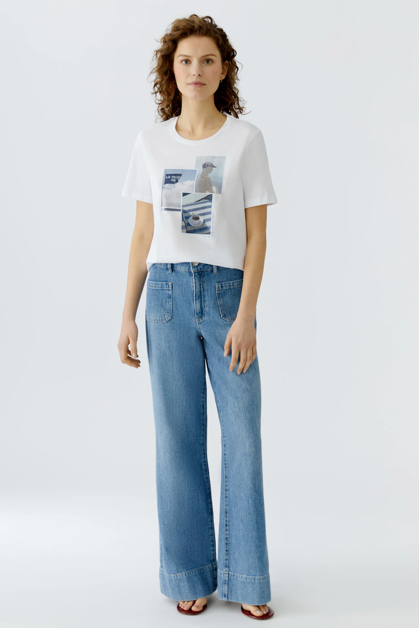 Damen-T-Shirt: Frau in weißem T-Shirt mit grafischem Print und lässigen Jeans steht entspannt.