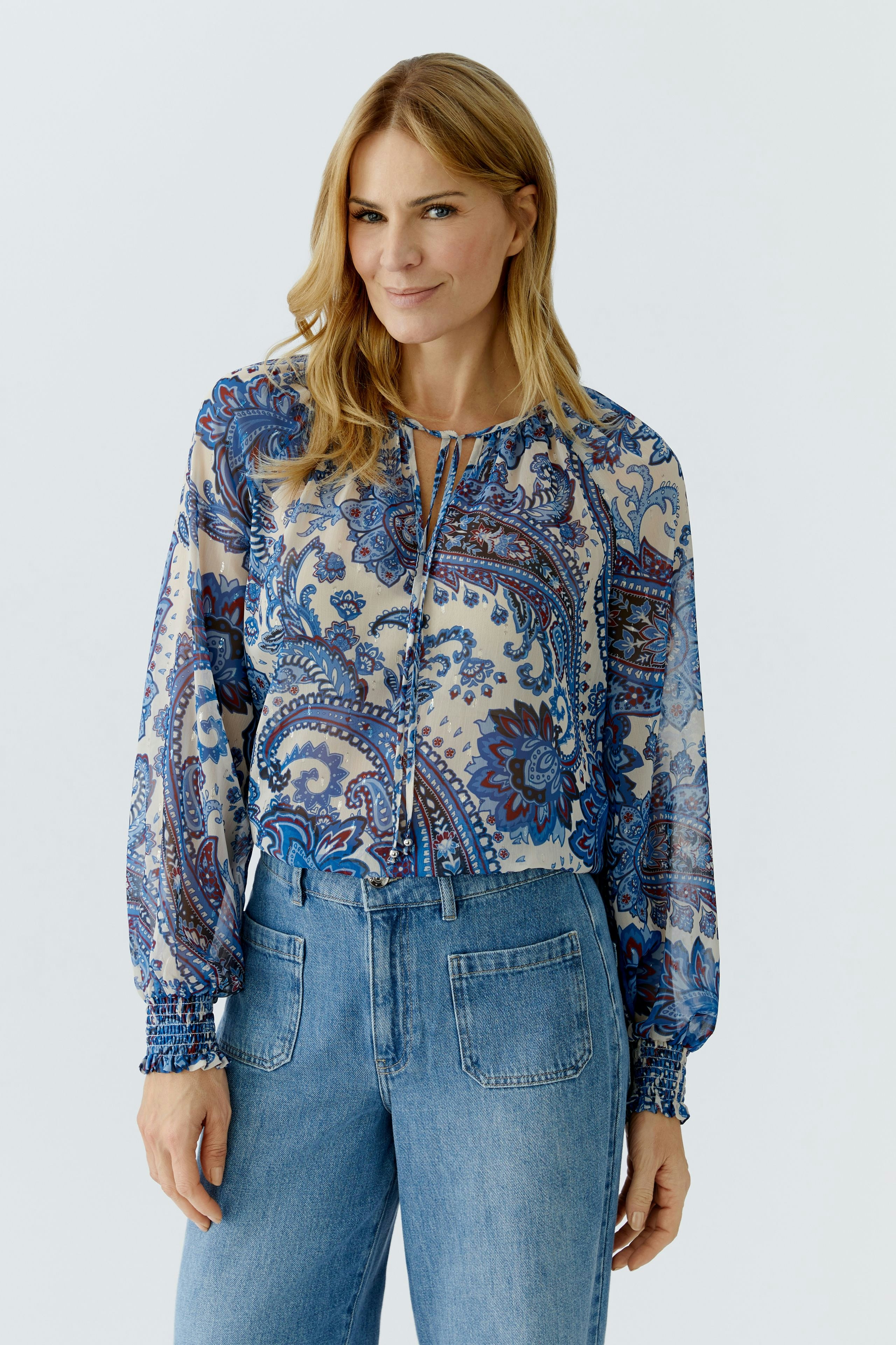 Lightweight blouse: Woman in a patterned blouse with balloon sleeves and relaxed fit jeans.