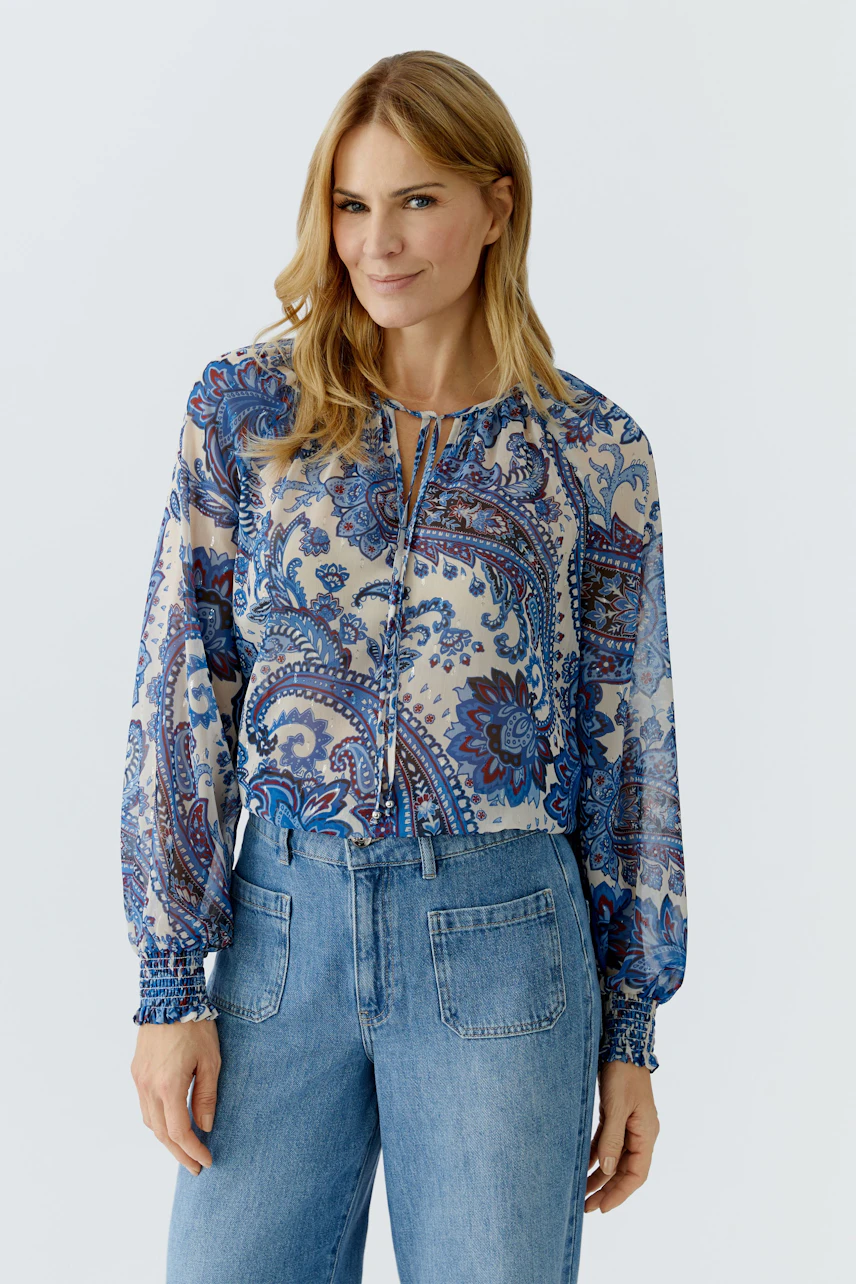 Lightweight blouse: Woman in a patterned blouse with balloon sleeves and relaxed fit jeans.