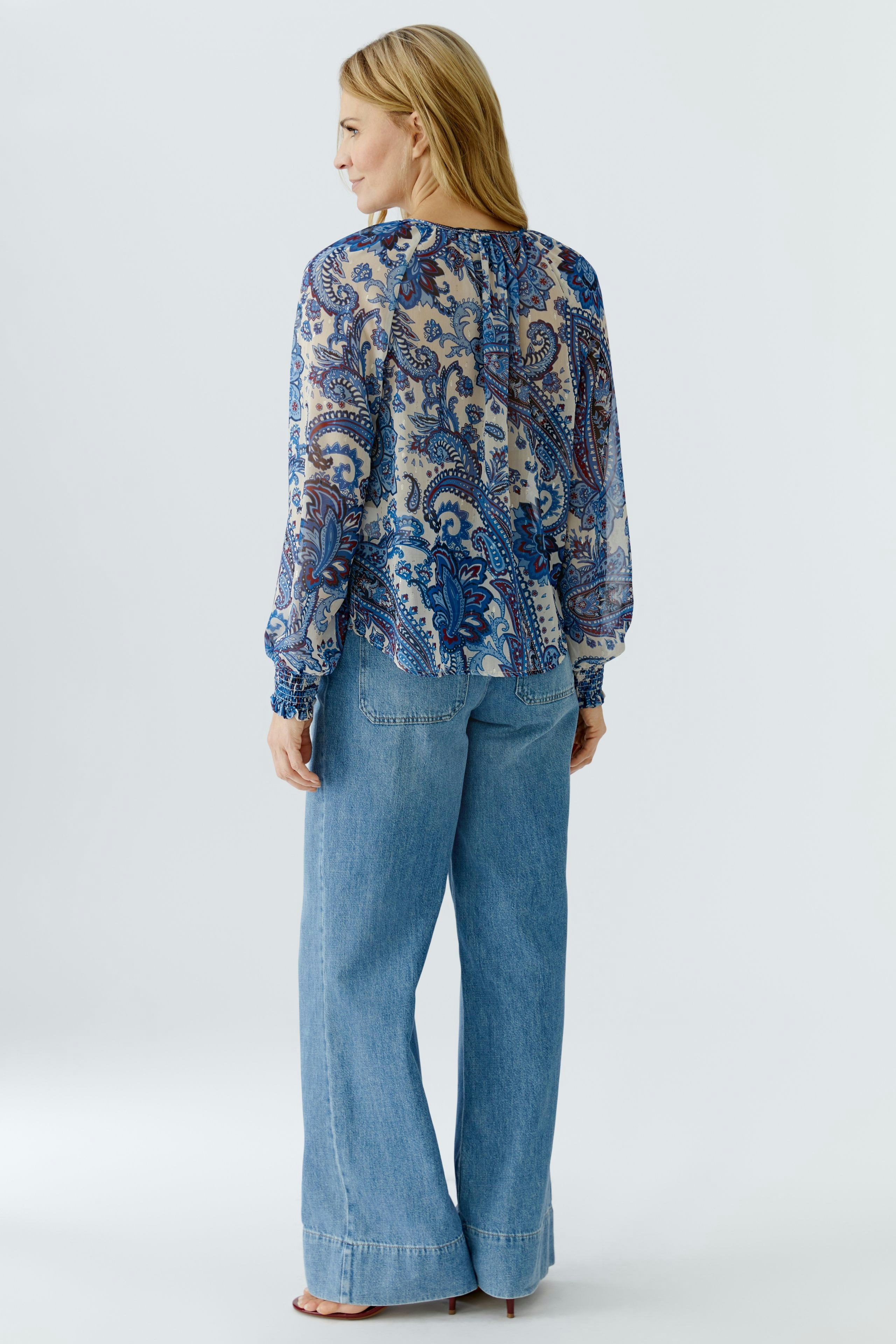 Lightweight blouse: Woman in a patterned blouse with billowy sleeves, paired with relaxed jeans.