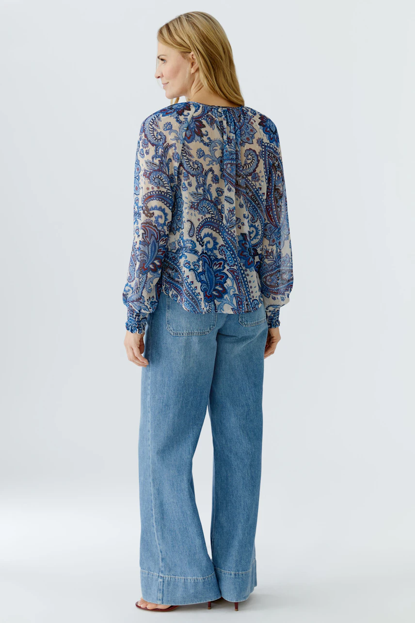 Lightweight blouse: Woman in a patterned blouse with billowy sleeves, paired with relaxed jeans.