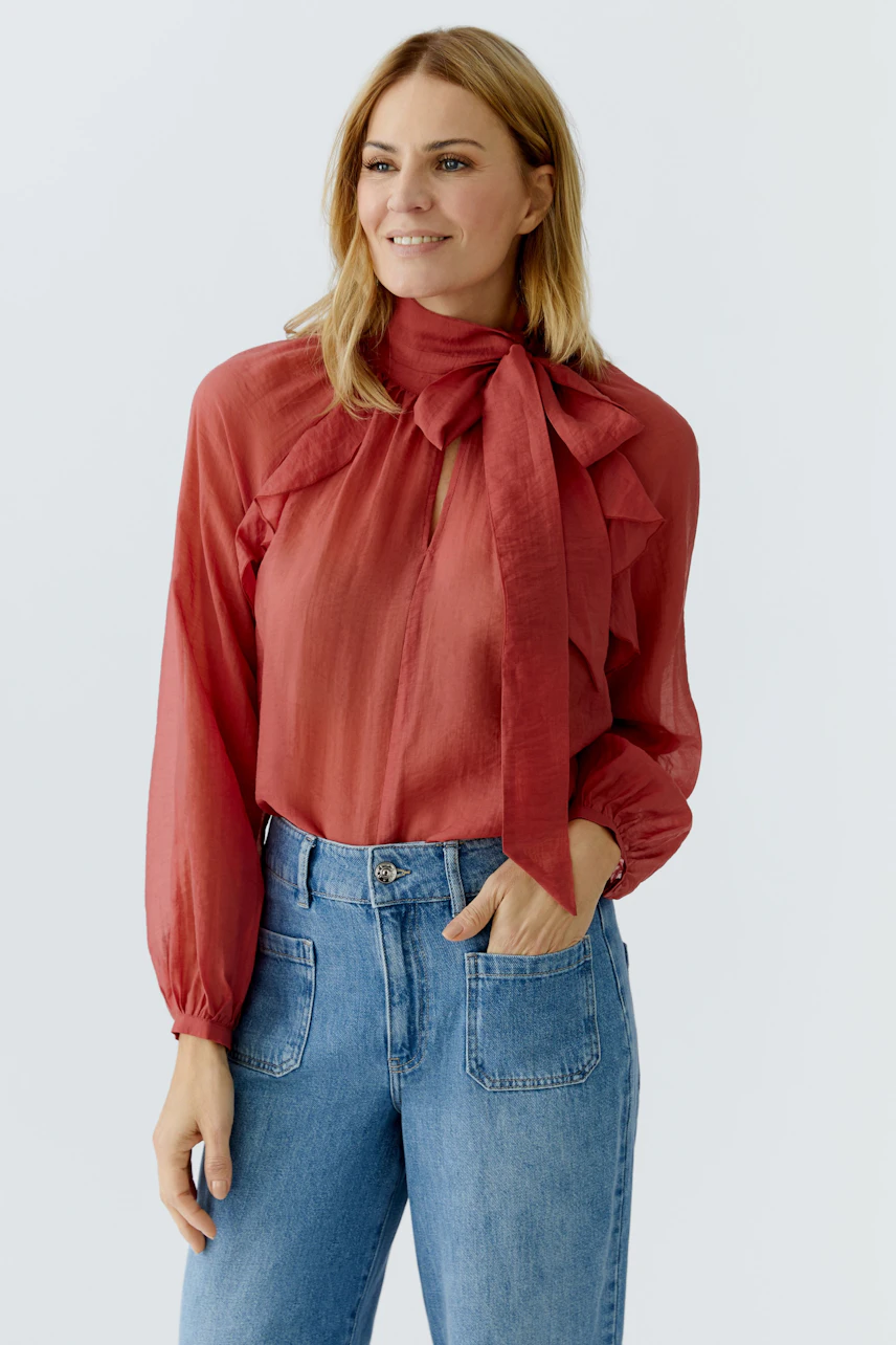 Rote Damen-Bluse mit Schleifenkragen und Rüschen, kombiniert mit lässigen Jeans.