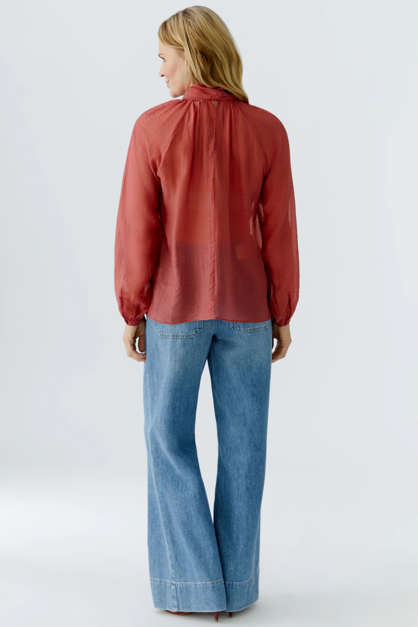 Damen-Bluse: Frau in transparenter, roter Bluse mit langen Ärmeln und lässigen Jeans.