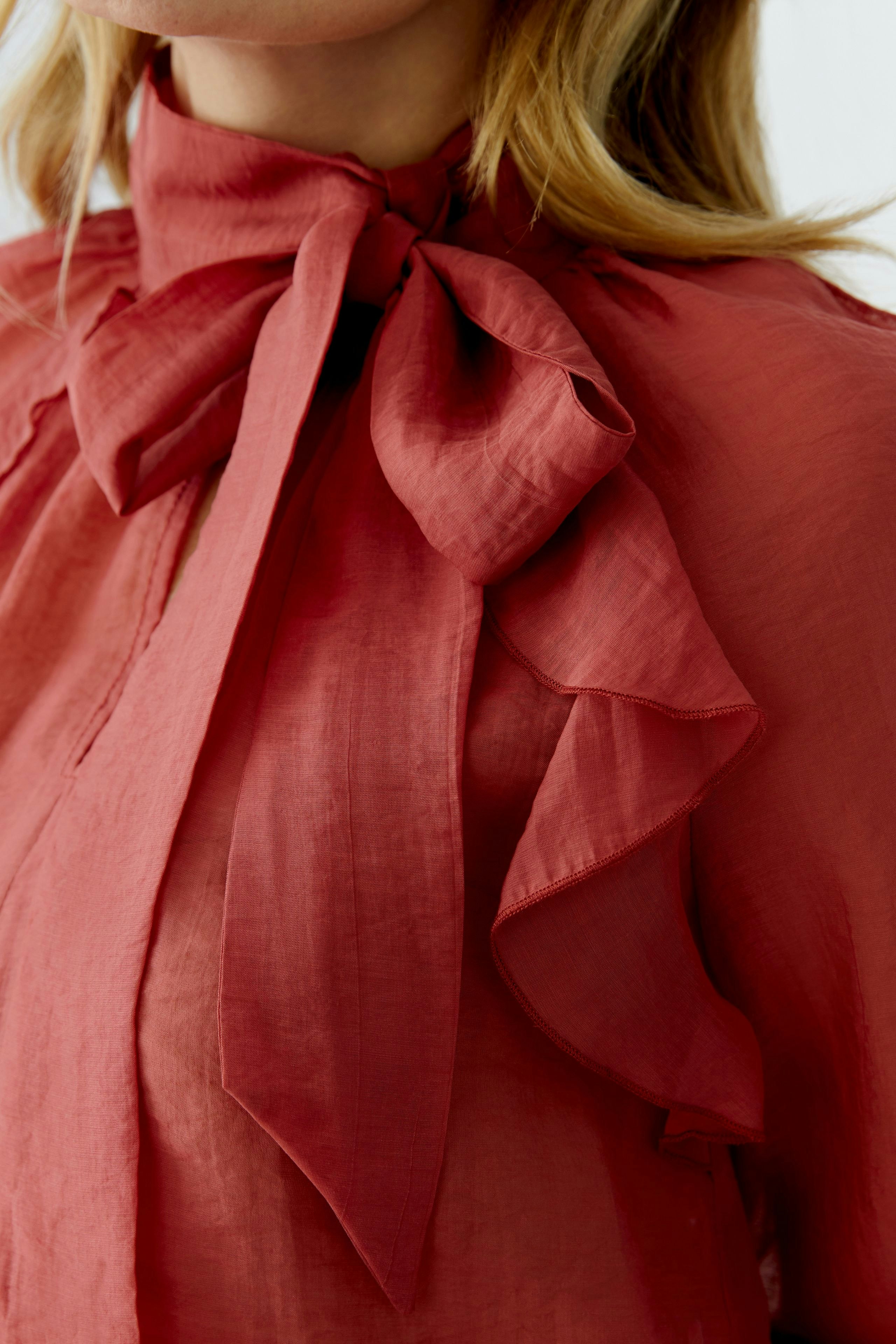 Stylish women's blouse with a bow tie detail and ruffled accents in a rich red hue.