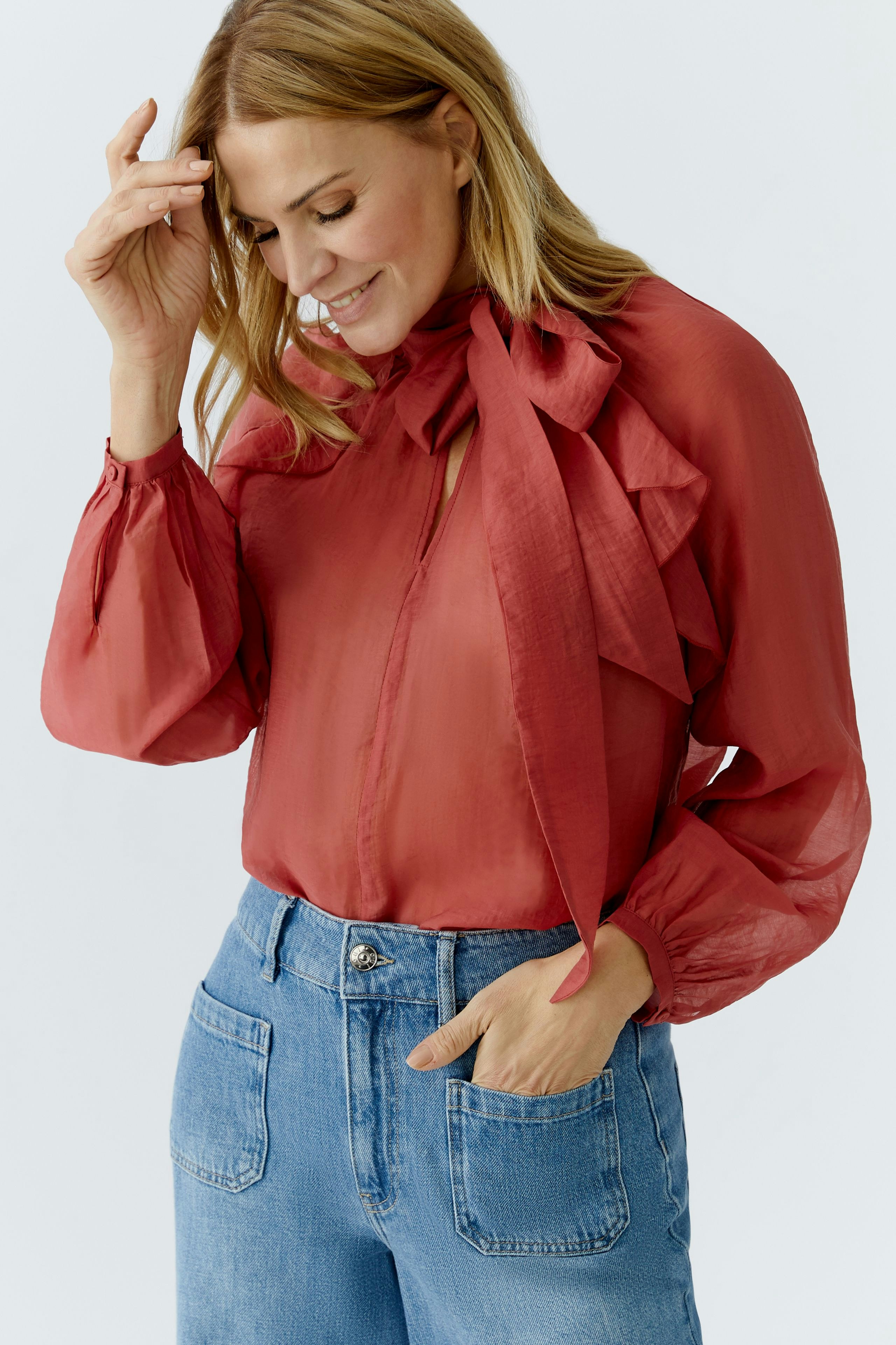 Stylish women's blouse in red with ruffled details, paired with casual denim.