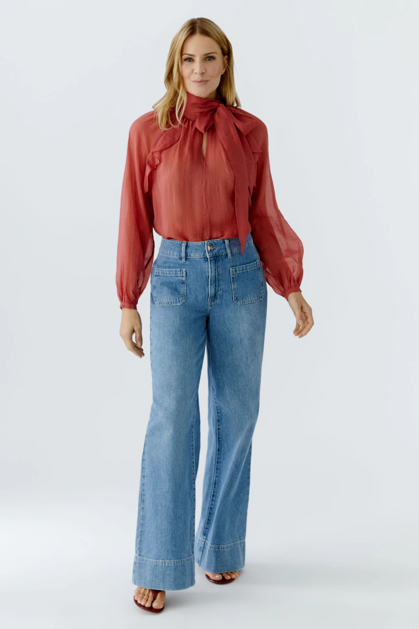 Damen-Bluse: Frau in roter Bluse mit Schleife und lässigen Jeans steht selbstbewusst.