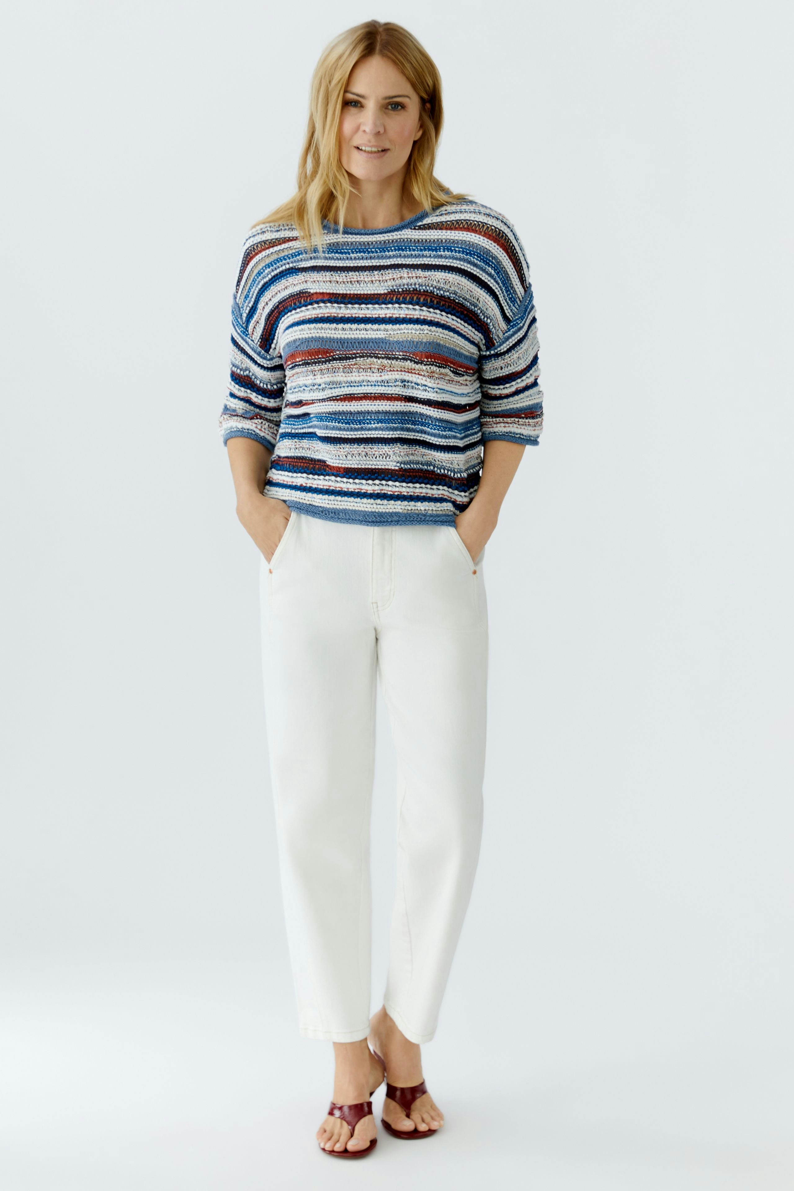 Casual women's pullover: Young woman in a striped pullover with relaxed fit and white pants.