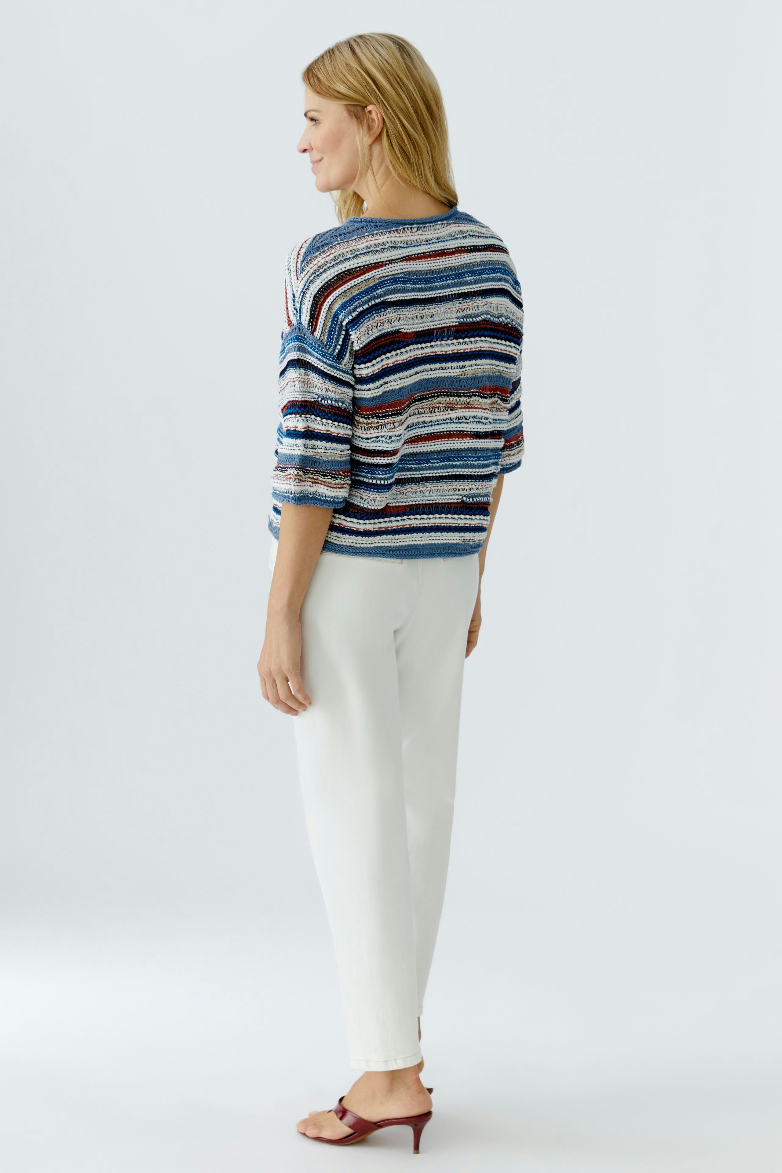 Casual women's pullover: A woman in a striped pullover with relaxed fit and light pants, viewed from the back.