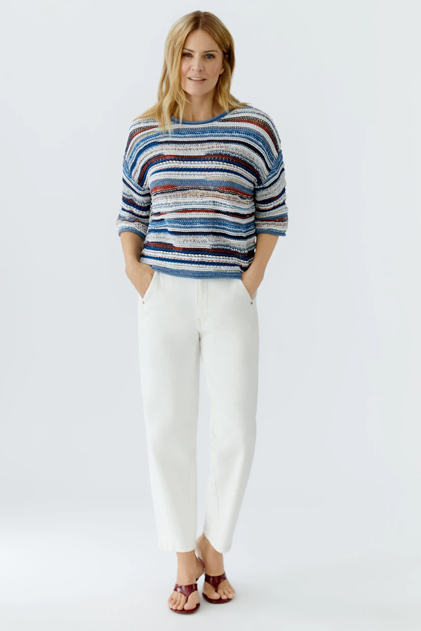 Casual women's pullover: Young woman in a striped pullover with relaxed fit and white pants.