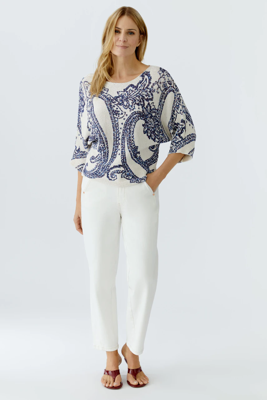 Damen-Pullover: Frau in lässigem, gemustertem Pullover mit weitem Schnitt und weißen Hosen.