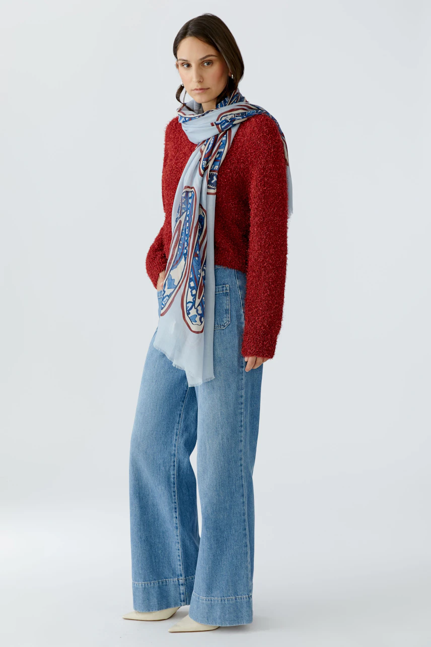 Damen-Schal: Frau trägt einen bunten Schal über einem roten Pullover und lässigen Jeans.