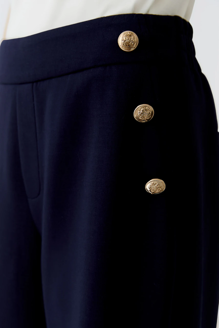 Moderne Damen-Hose: Detailaufnahme einer Frau in navyfarbener Hose mit goldenen Knöpfen.