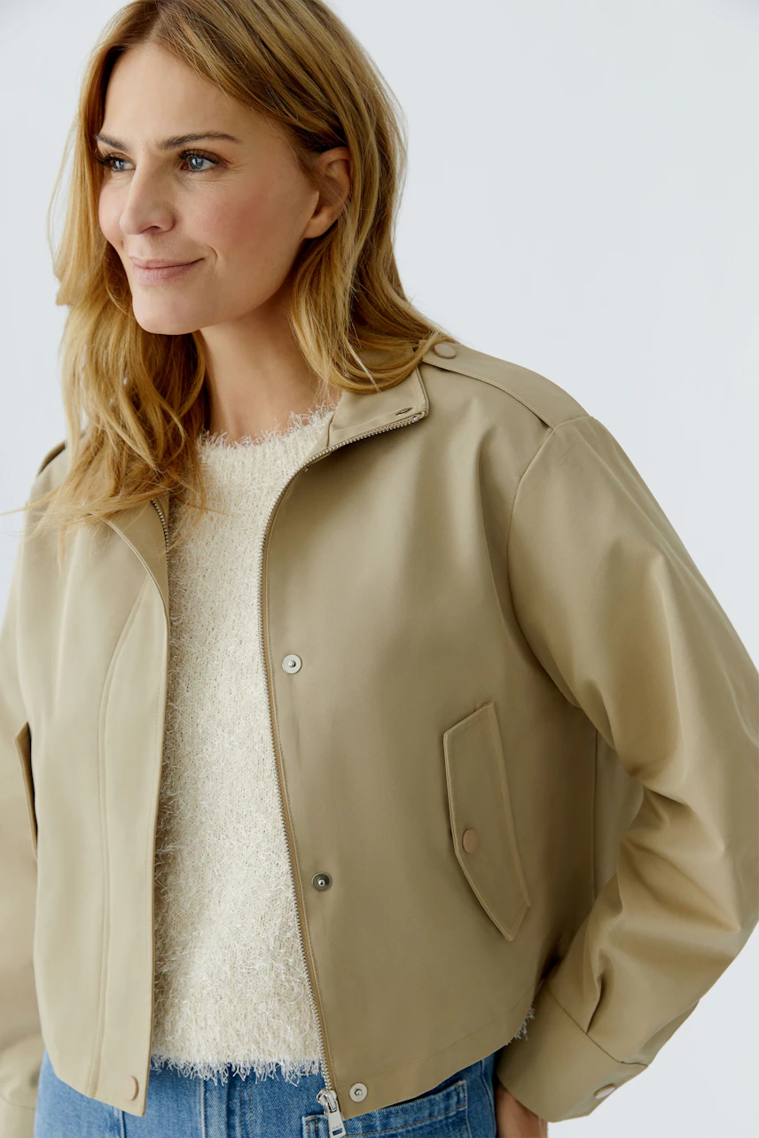 Casual women's blouson: Woman in a beige bomber jacket over a cozy pullover, smiling confidently.