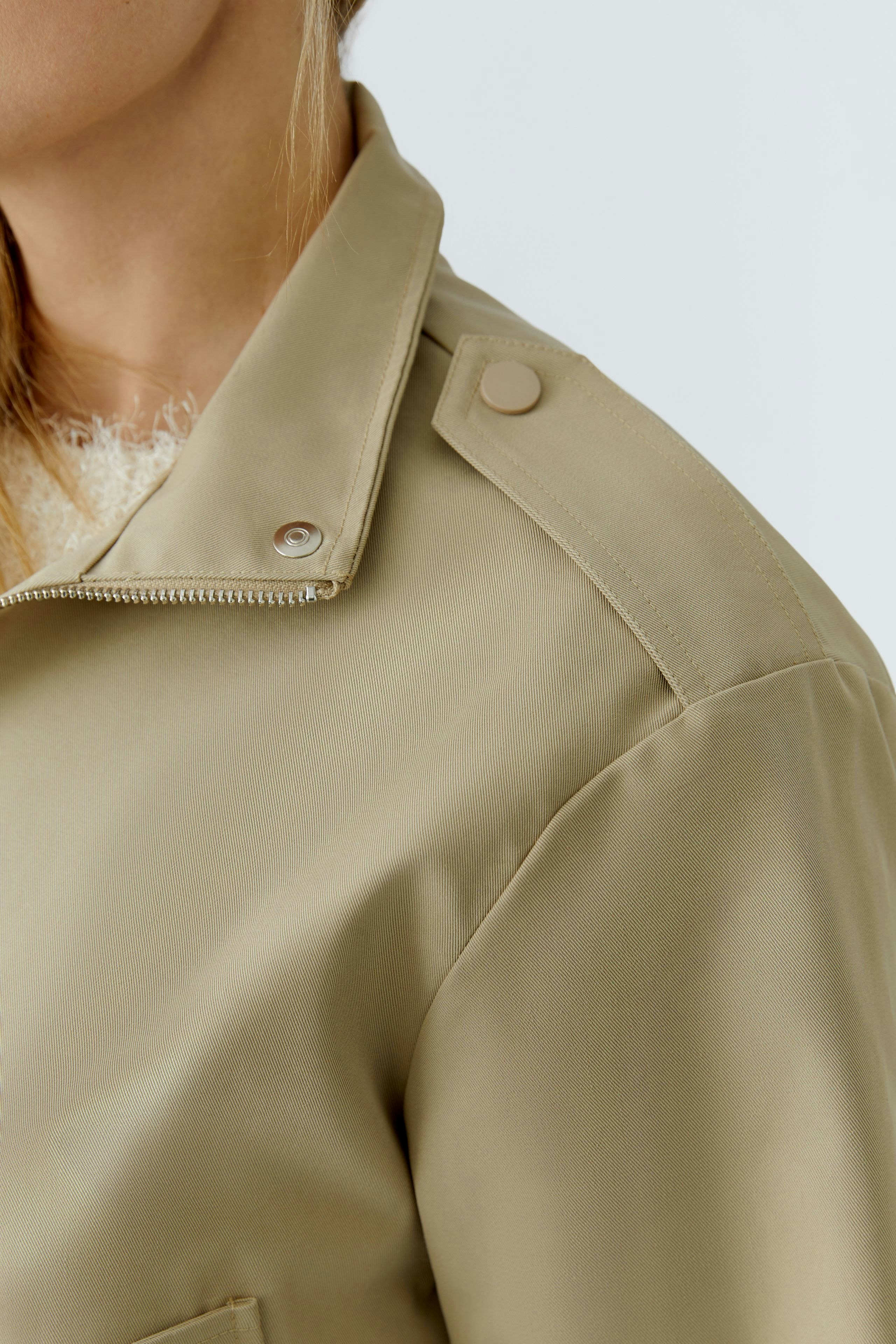 Stylish women's blouson: Close-up of a woman in a beige jacket with a modern design and button details.