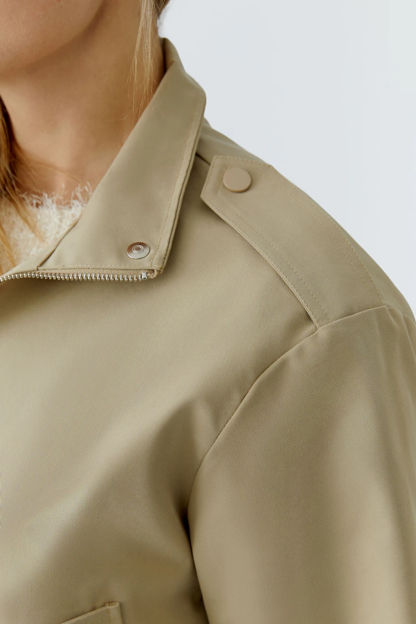 Stylish women's blouson: Close-up of a woman in a beige jacket with a modern design and button details.