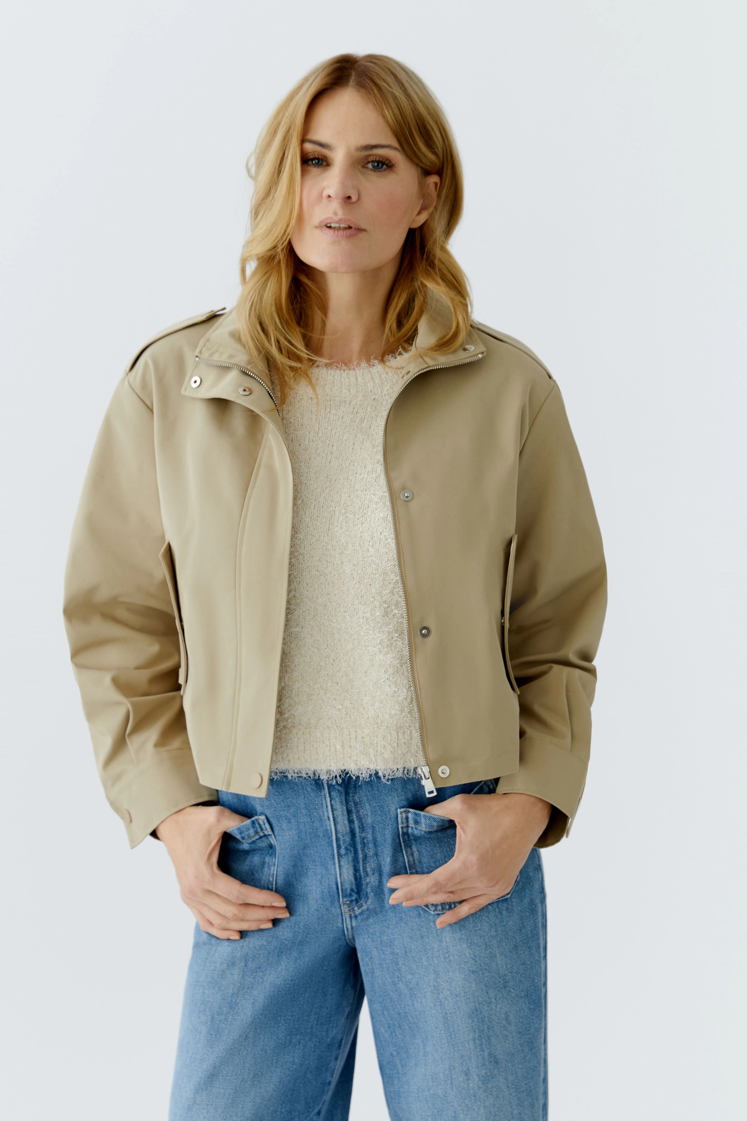 Beiger Blouson: Frau in lässiger Jacke mit weichem Pullover und Jeans, schaut direkt in die Kamera.