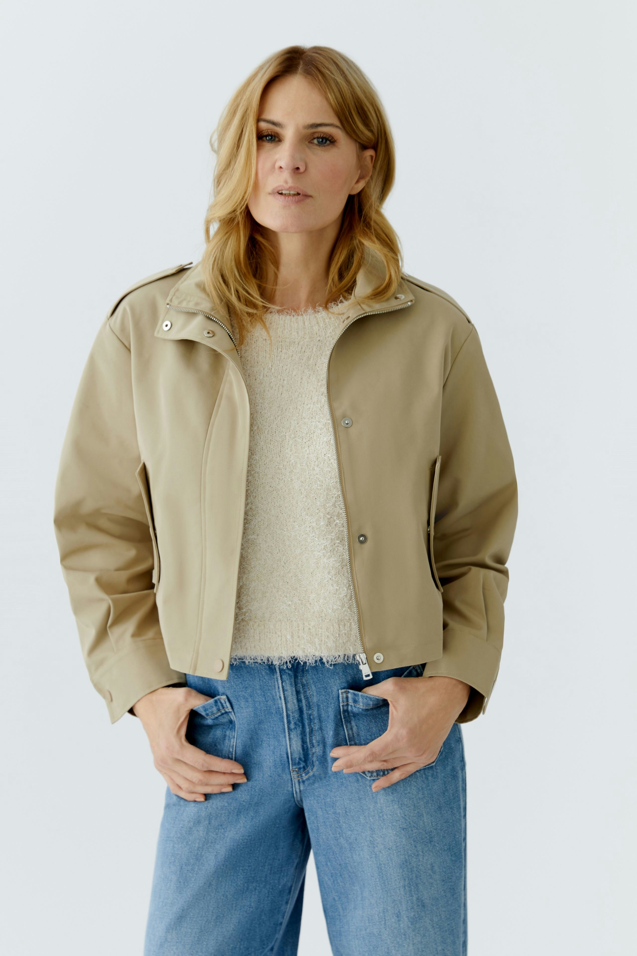 Casual women's blouson: Woman in a beige jacket over a cozy pullover and jeans, looking confidently.