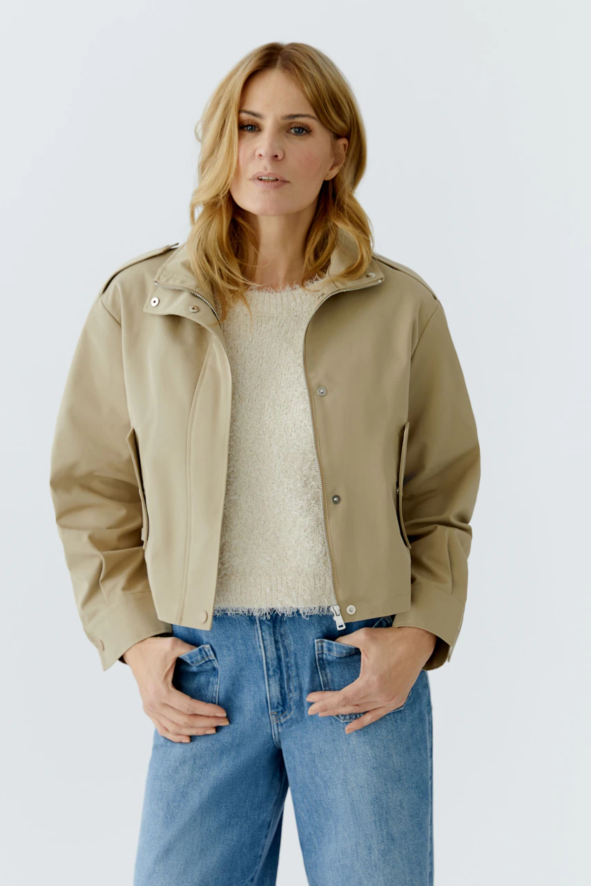 Casual women's blouson: Woman in a beige jacket over a cozy pullover and jeans, looking confidently.