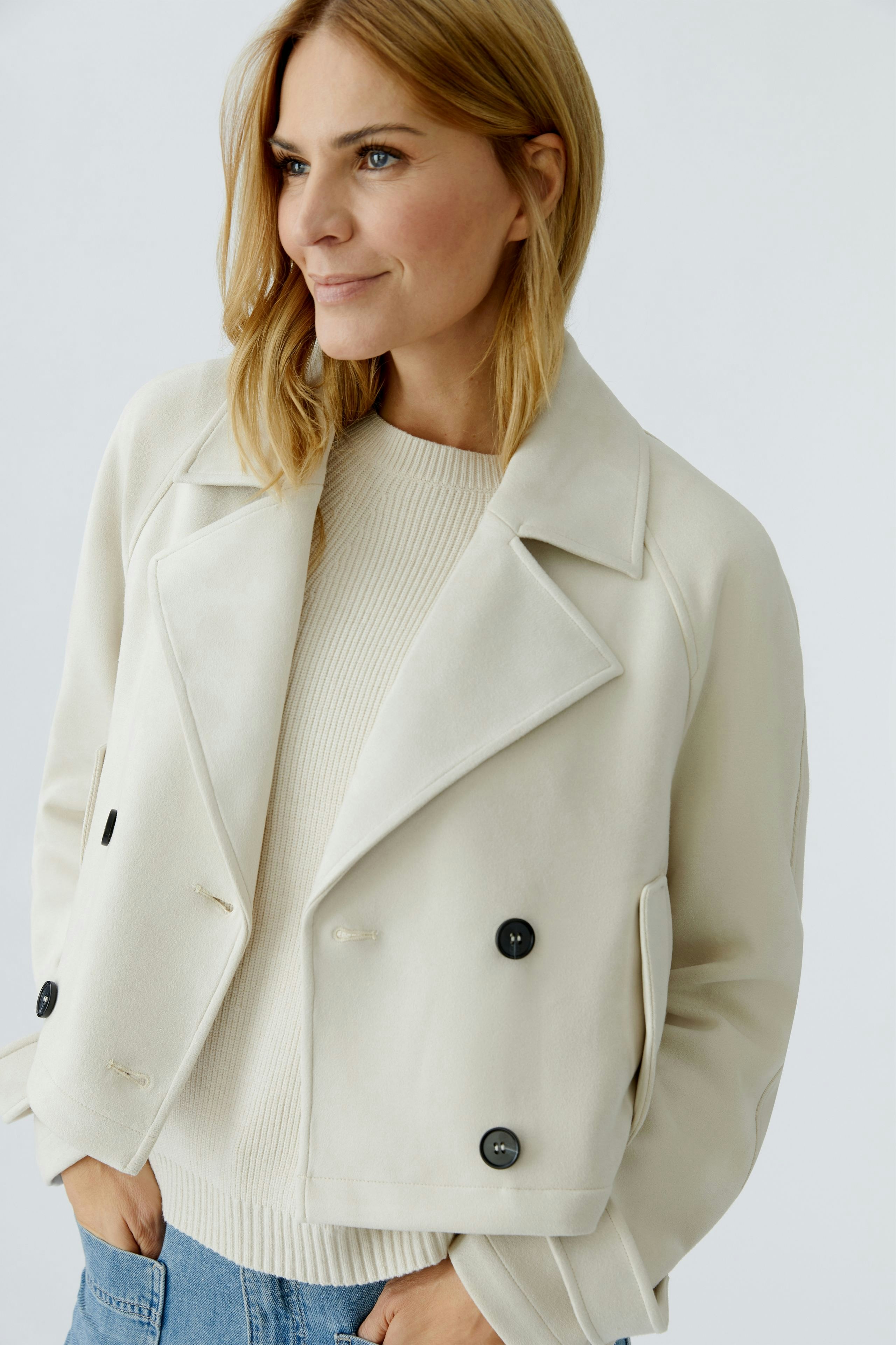 Stylish women's faux leather jacket: A woman in a cream jacket with black buttons, paired with a light pullover.