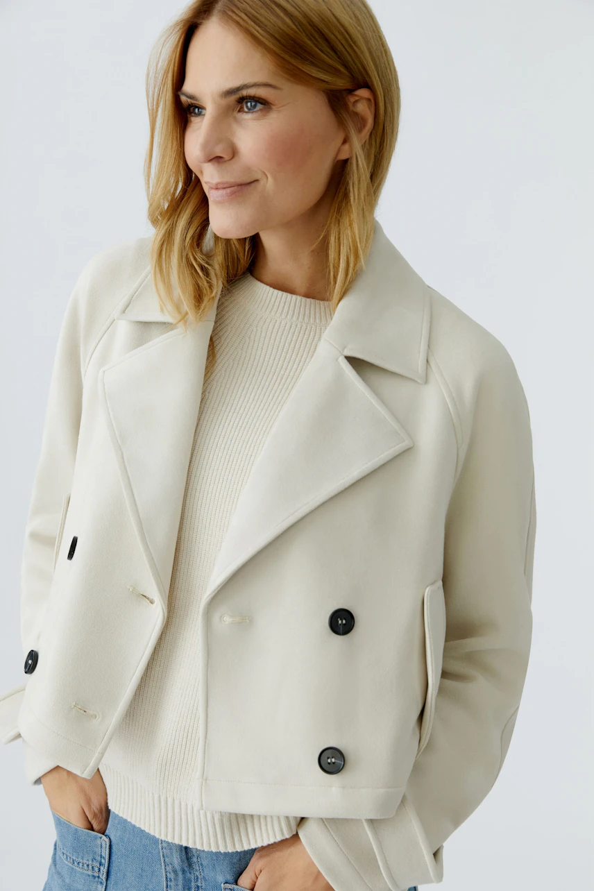 Stylish women's faux leather jacket: A woman in a cream jacket with black buttons, paired with a light pullover.