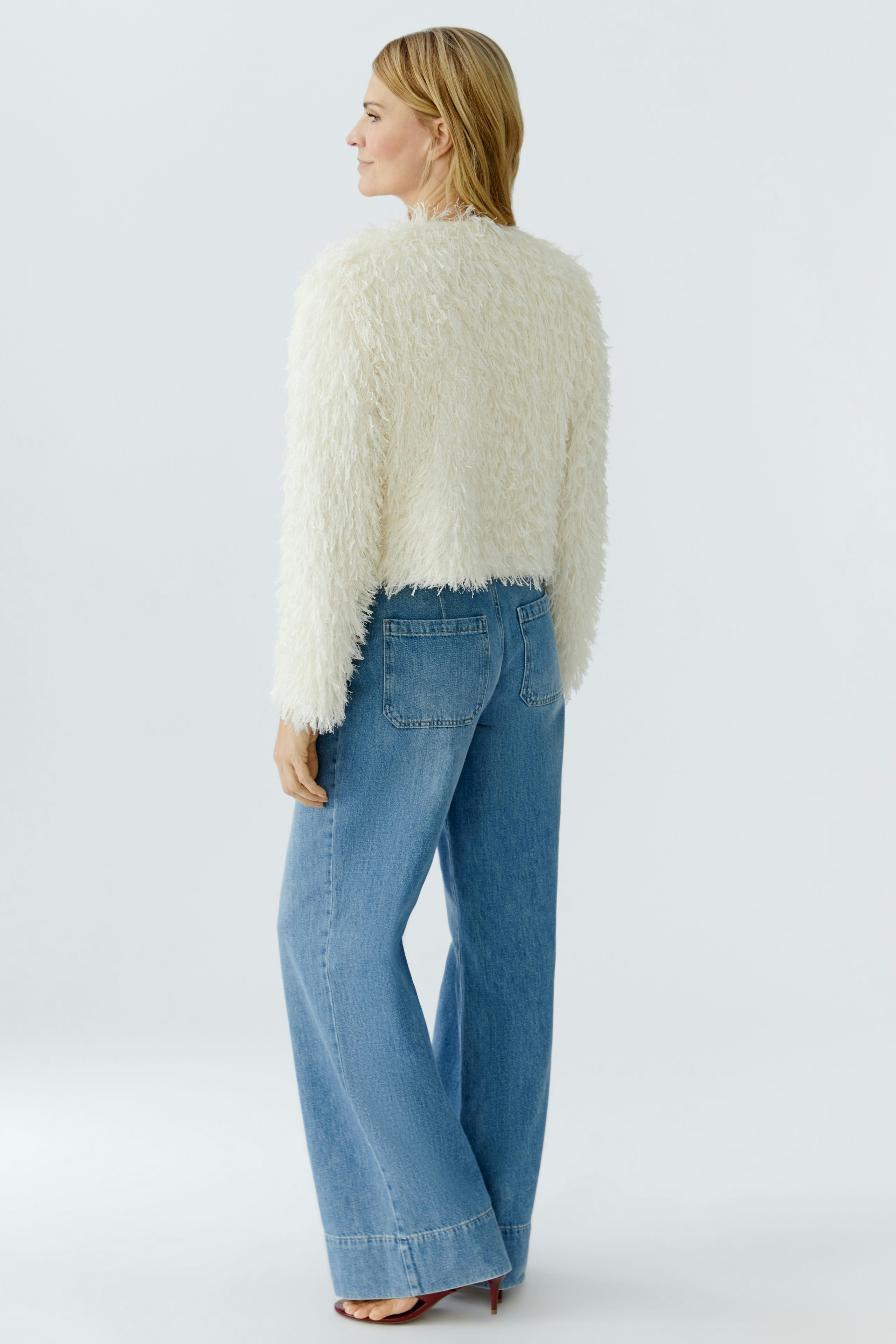 Cozy women's jacket: A woman in a fluffy white jacket paired with wide-leg jeans.