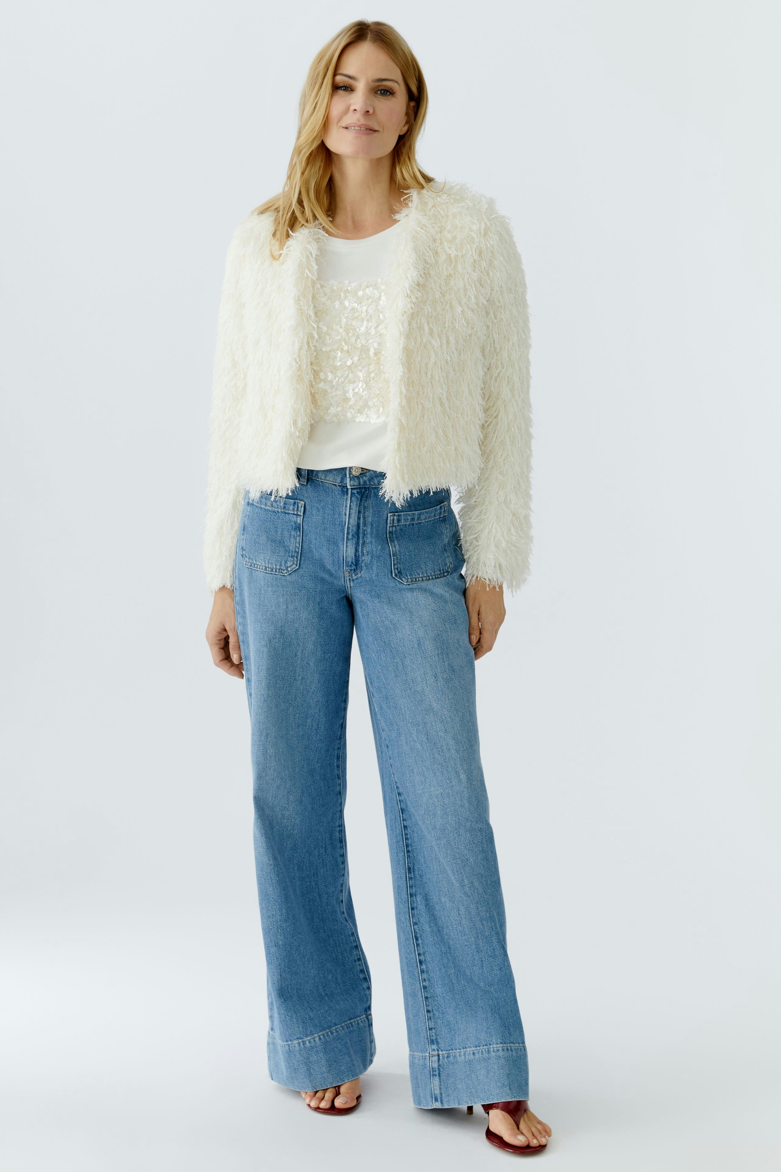 Flauschige Damen-Jacke: Frau in weißer, weicher Jacke mit lässigem Look und Jeans steht entspannt.