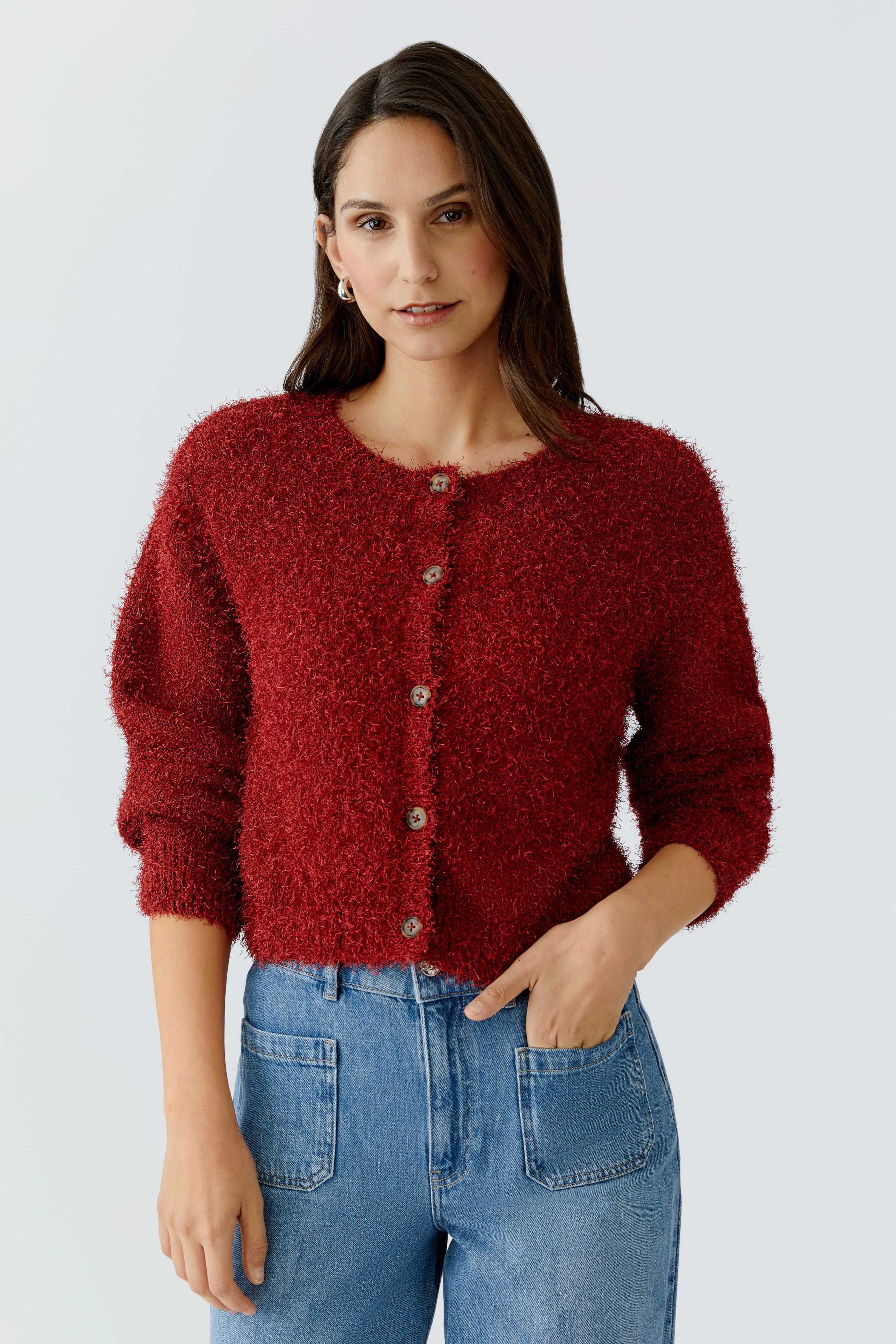 Rote Strickjacke: Junge Frau trägt eine kuschelige, rote Strickjacke mit Knöpfen und lässigen Jeans.