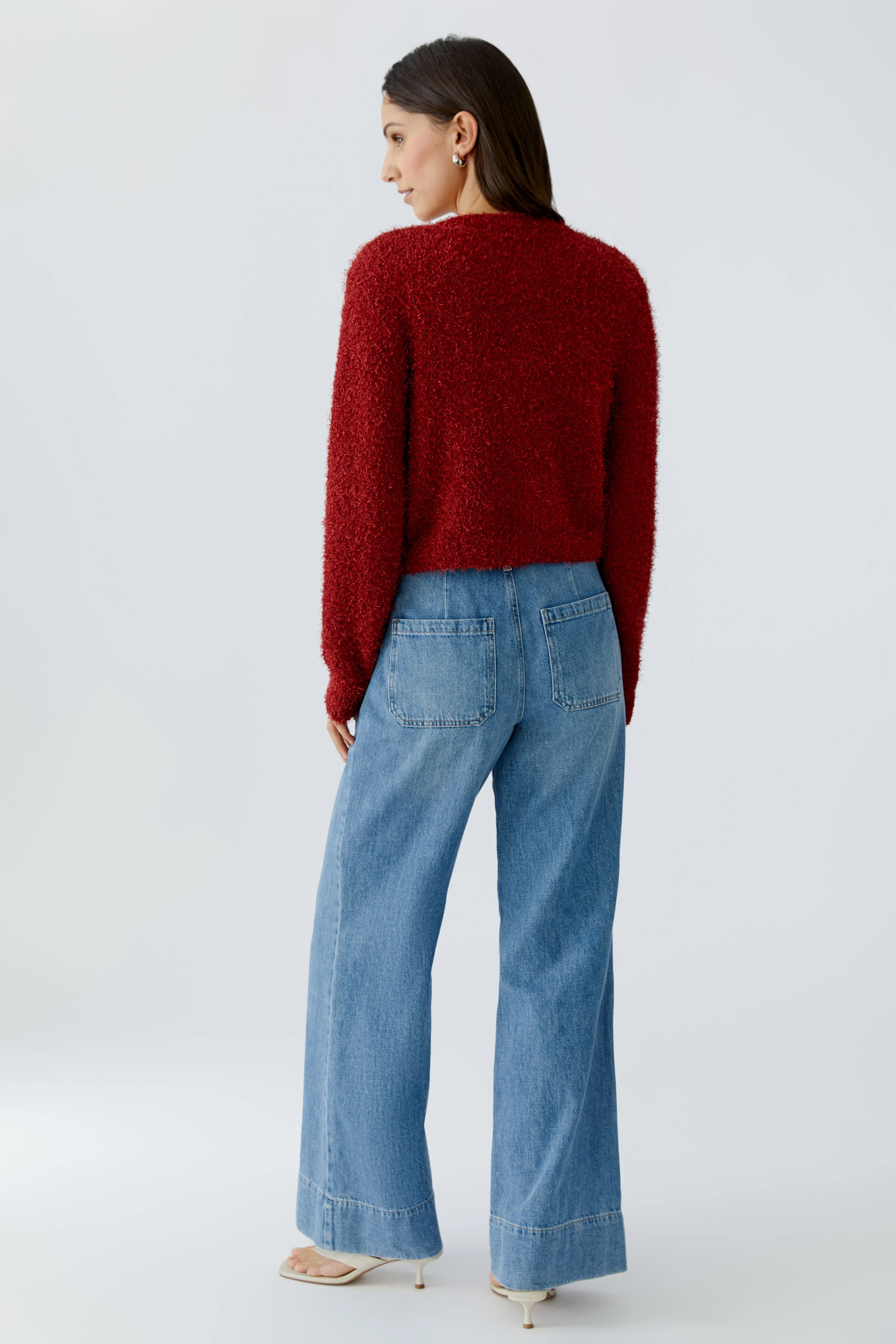 Rote Damen-Strickjacke: Frau mit lockigem Haar trägt eine kuschelige, rote Strickjacke und weite Jeans.