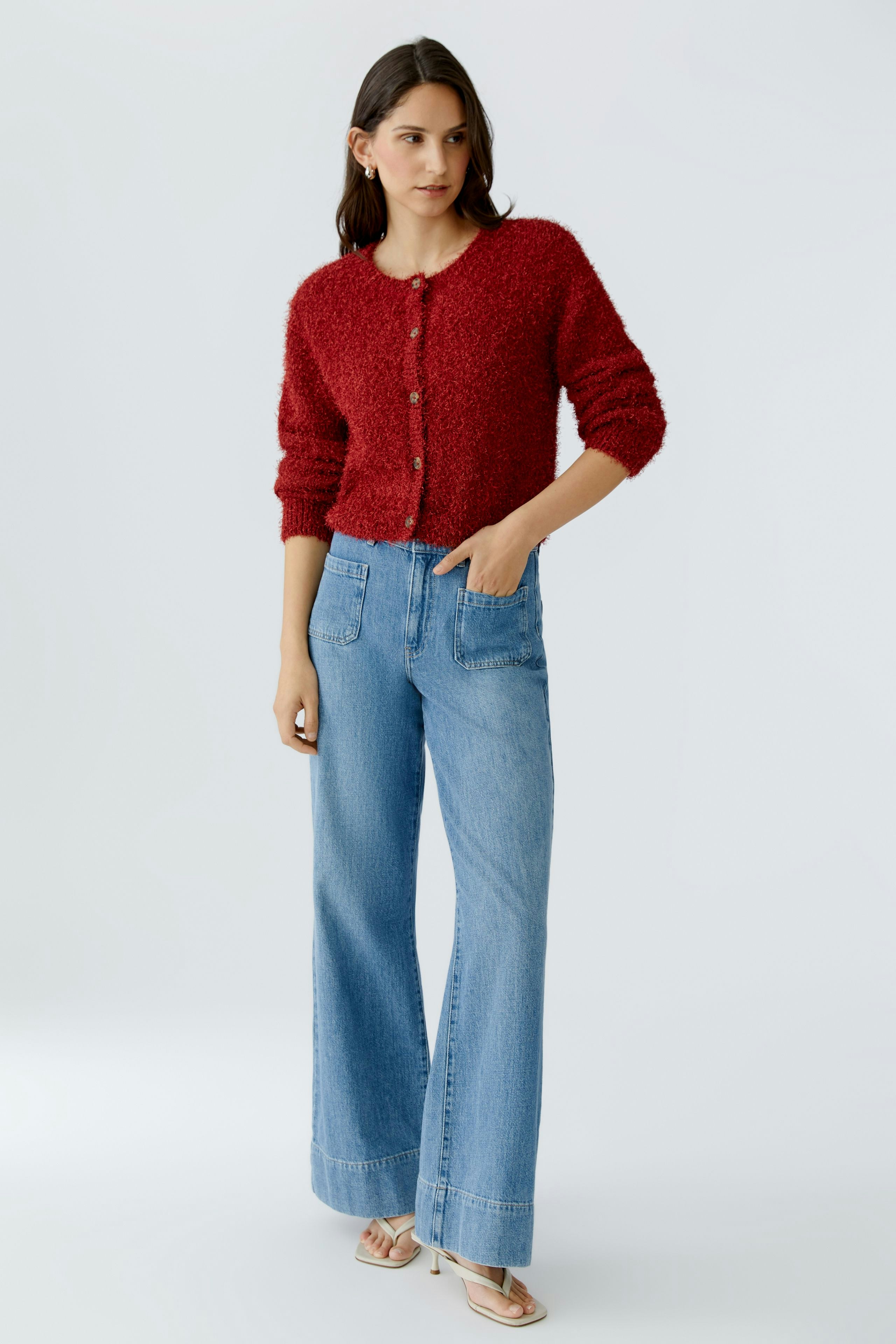 Cozy women's cardigan: A woman in a red fluffy cardigan paired with wide-leg jeans.