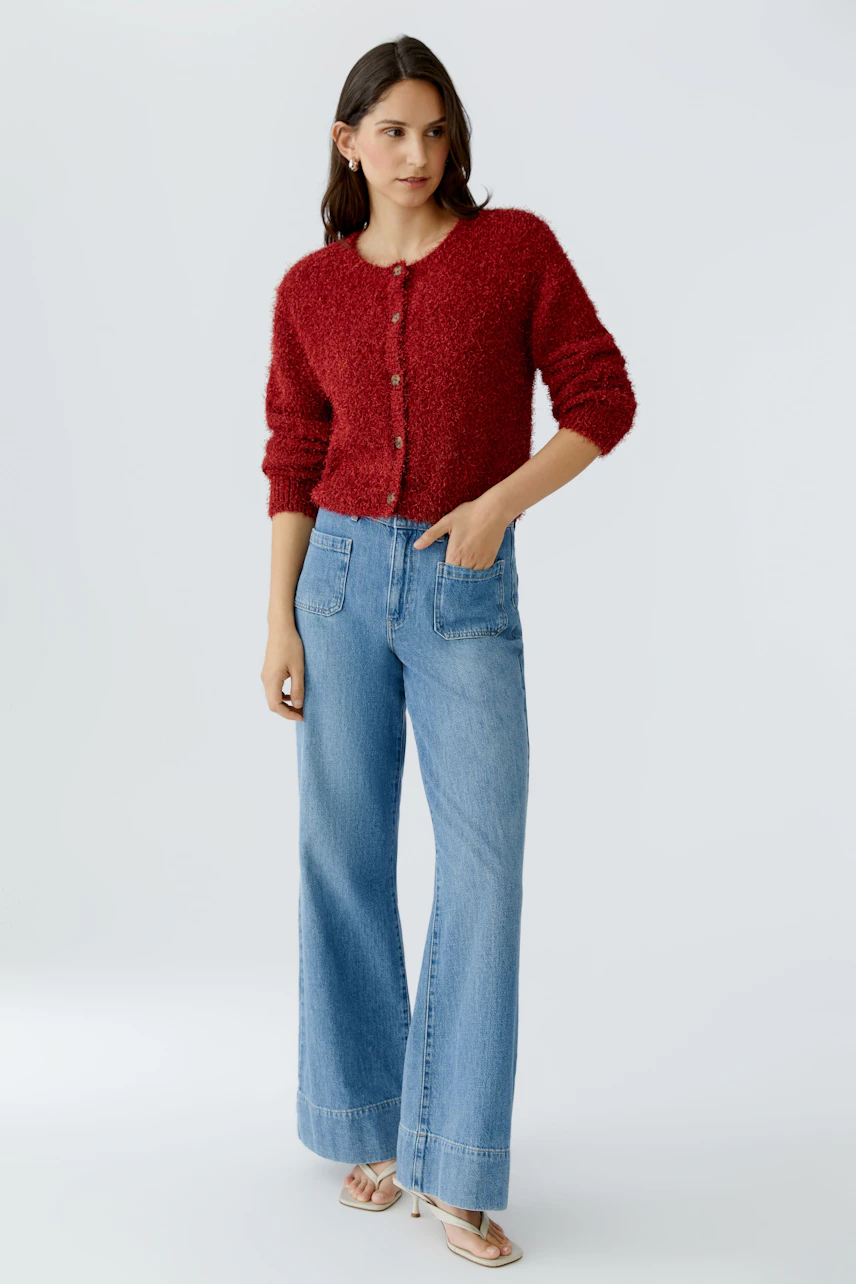 Cozy women's cardigan: A woman in a red fluffy cardigan paired with wide-leg jeans.