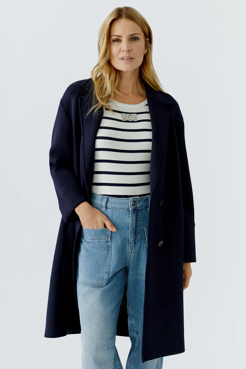 Damen-Mantel: Frau in navyfarbenem Mantel über gestreiftem Shirt und Jeans, lässig mit einer Hand in der Tasche.
