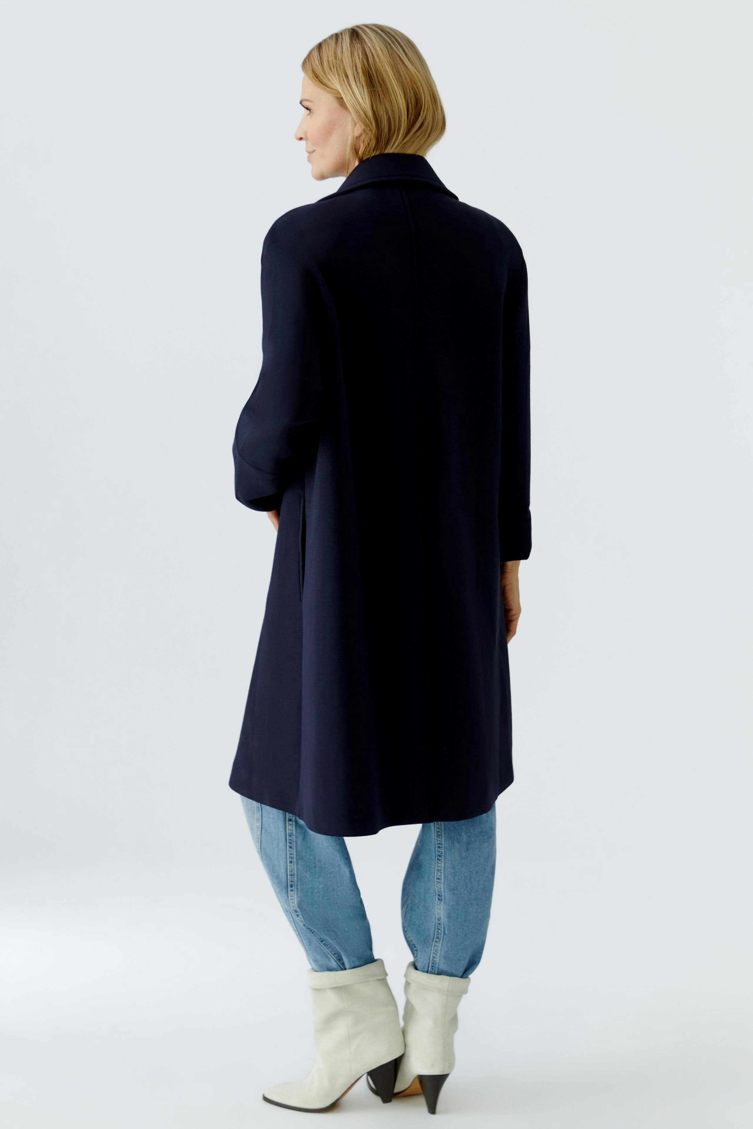 Stylish women's coat: A woman in a navy coat with a relaxed fit, paired with light blue jeans.