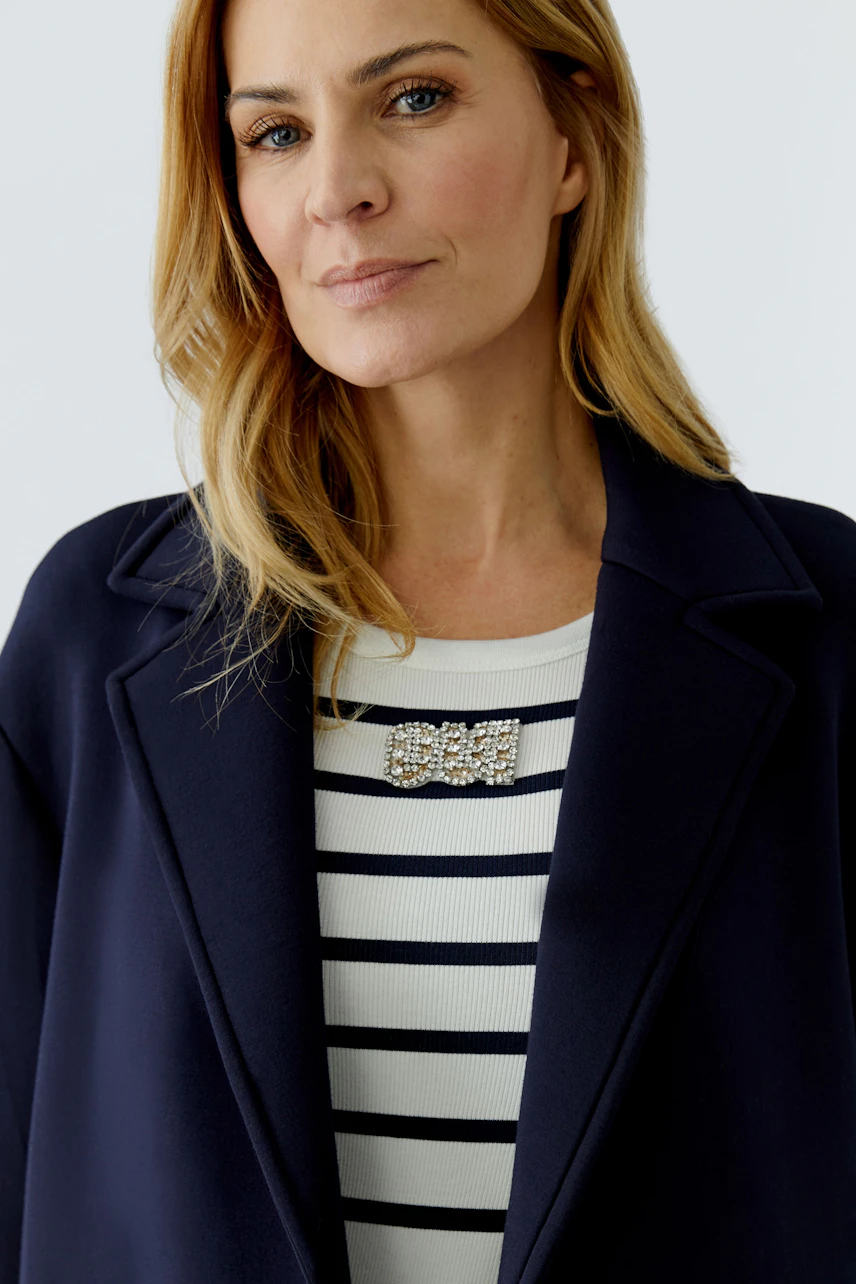 Damen-Mantel: Frau mit blauer Jacke über gestreiftem Pullover, lächelt selbstbewusst in die Kamera.