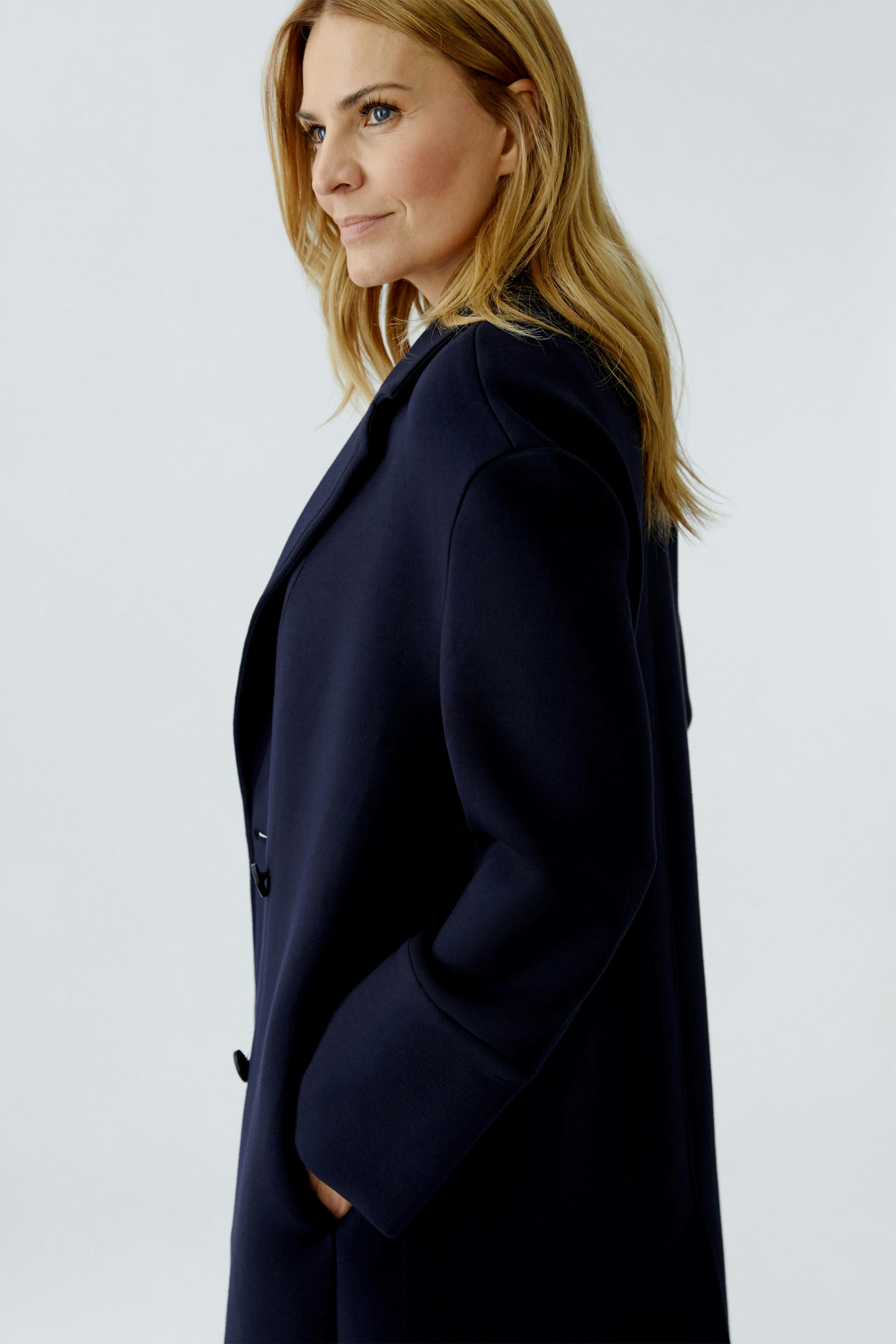 Modern women's coat: A woman in a navy coat with pockets, showcasing a relaxed and stylish look.