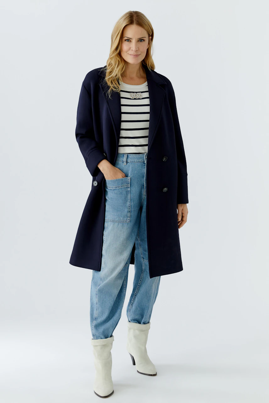 Damen-Mantel: Frau in navyfarbenem Mantel über gestreiftem Shirt und lässigen Jeans.