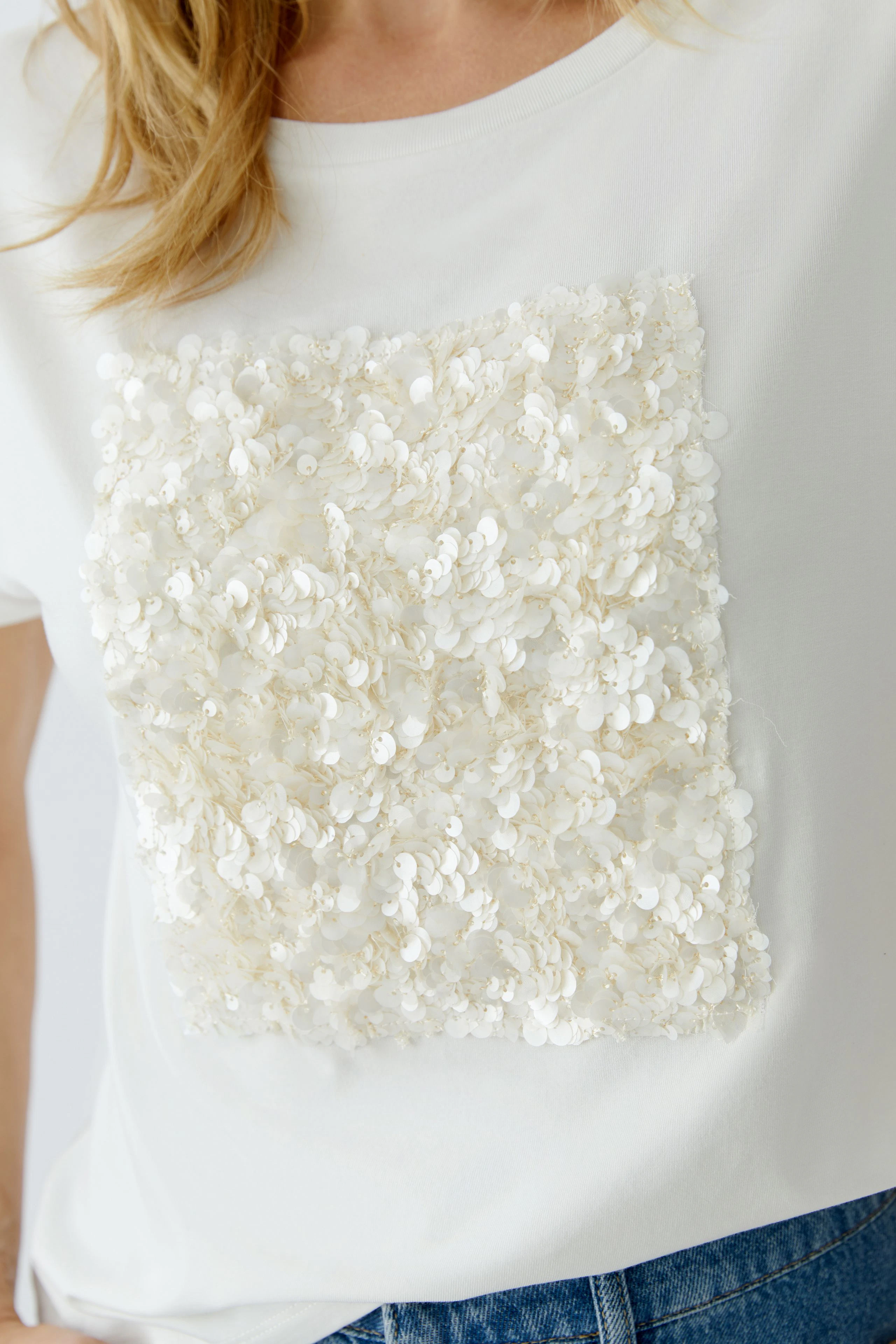 Damen-T-Shirt: Frau trägt ein weißes Shirt mit glitzerndem Pailletten-Design auf der Vorderseite.