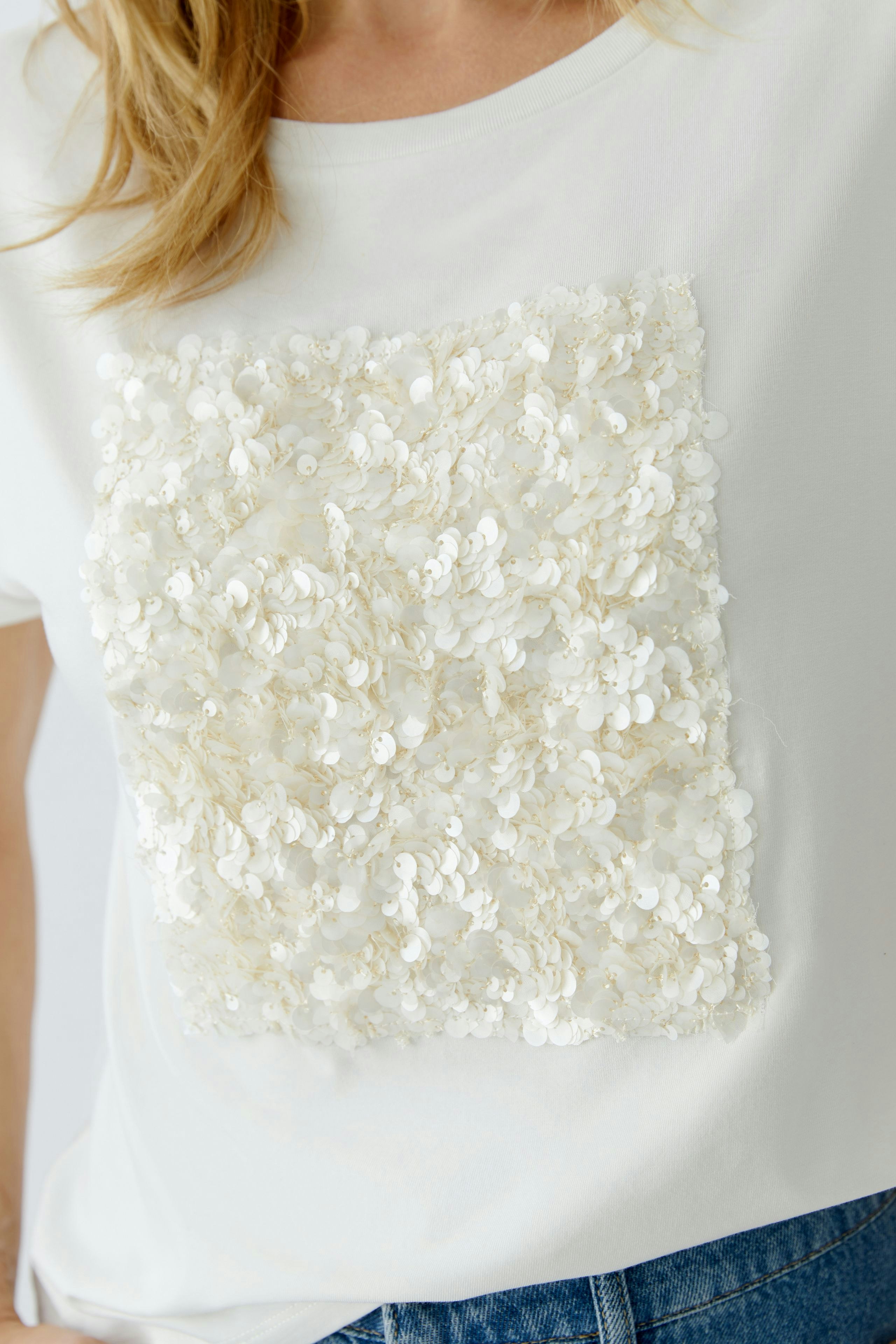 Casual women's T-shirt: Close-up of a woman wearing a white top with a textured sequin design.