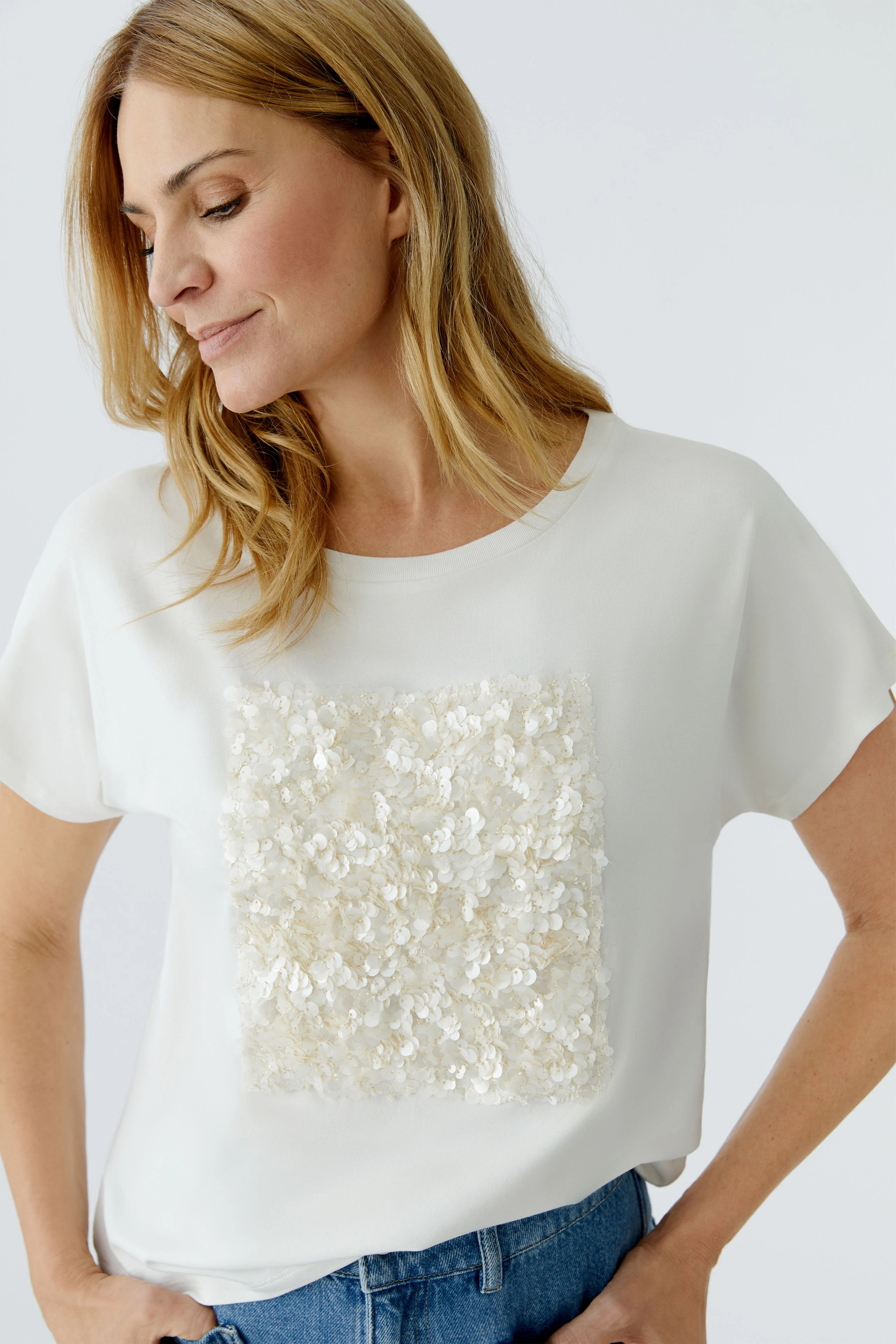 Damen-T-Shirt: Frau in weißem Shirt mit floralem Design, lässig kombiniert mit Jeans.