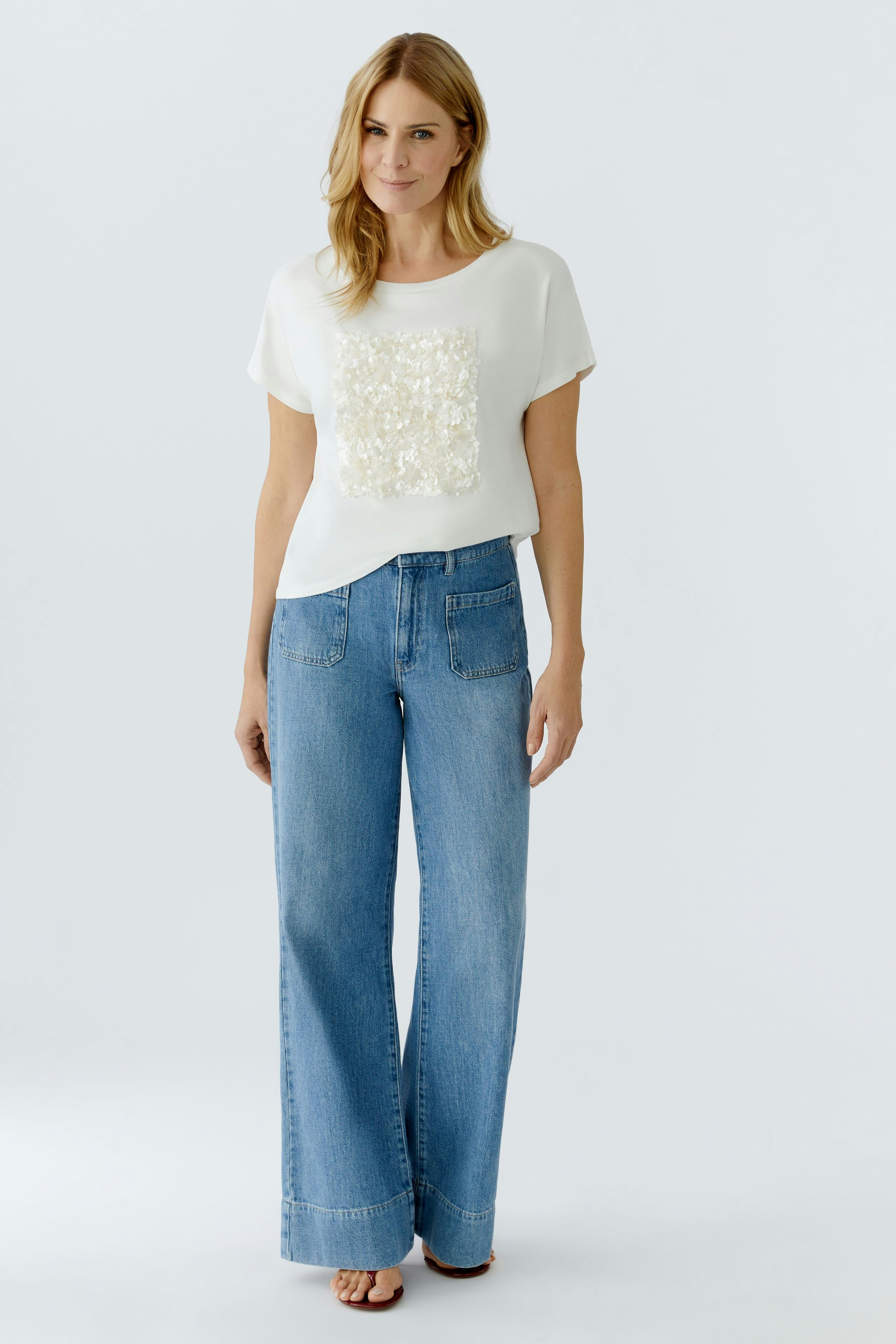 Damen-T-Shirt: Frau trägt ein weißes T-Shirt mit dekorativem Element und lässigen Jeans.