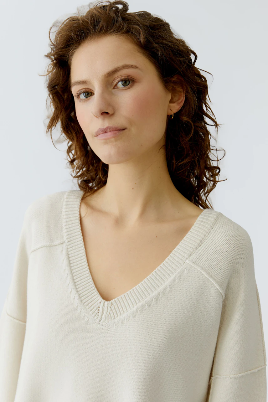 Casual women's pullover: A woman in a cream V-neck pullover with a relaxed fit.