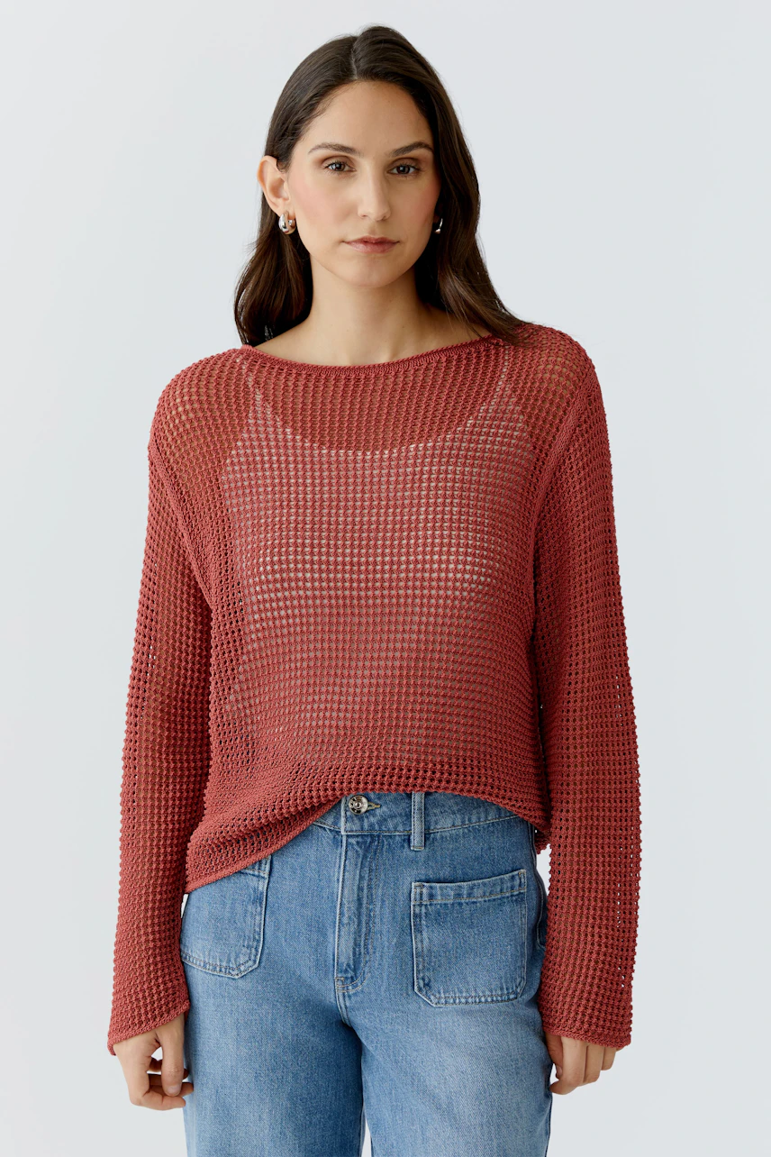 Casual women's pullover: Young woman in a loose-knit rust pullover paired with blue jeans.