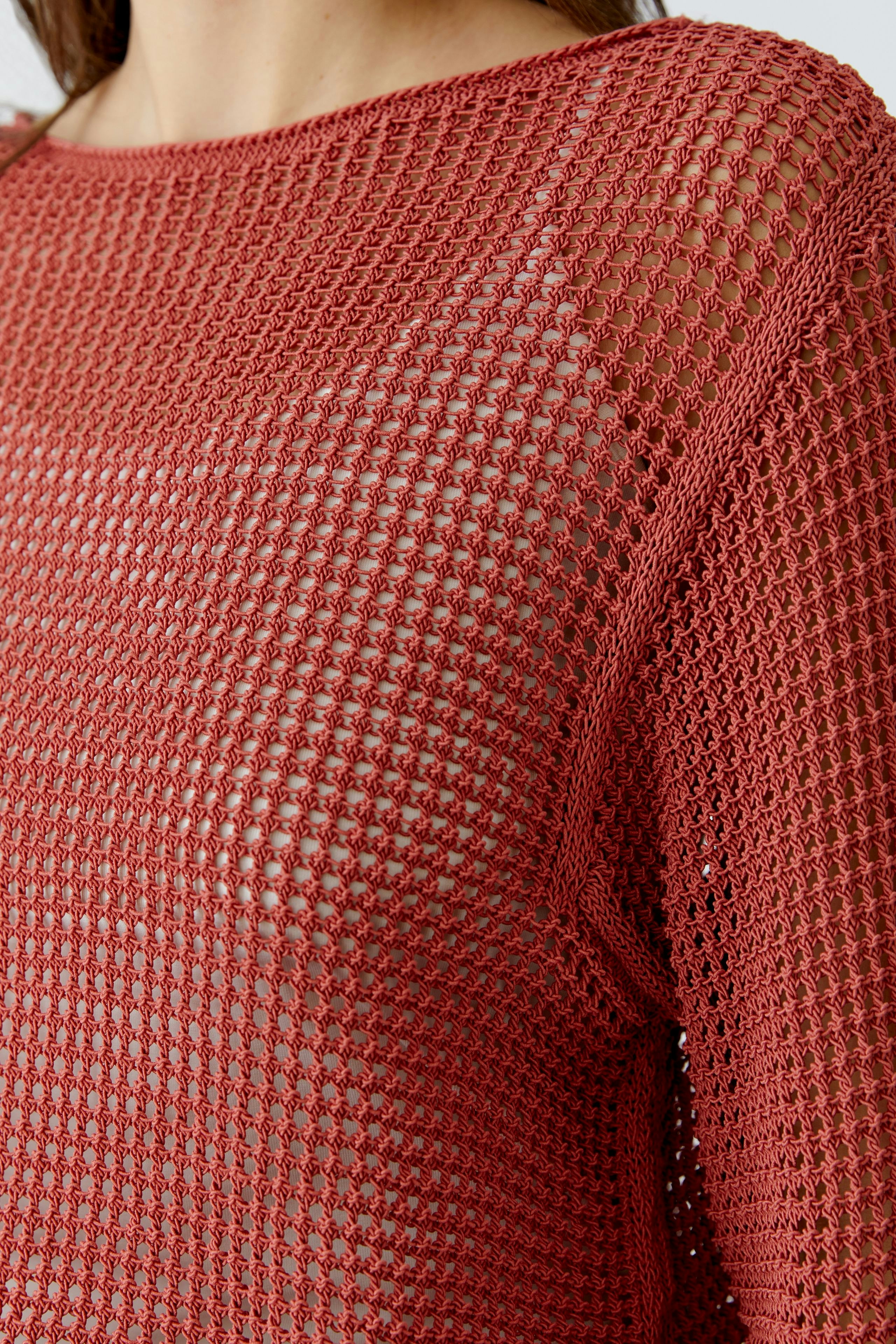 Casual women's pullover: Close-up of a woman in a loose-knit, rust-colored pullover with an open weave.
