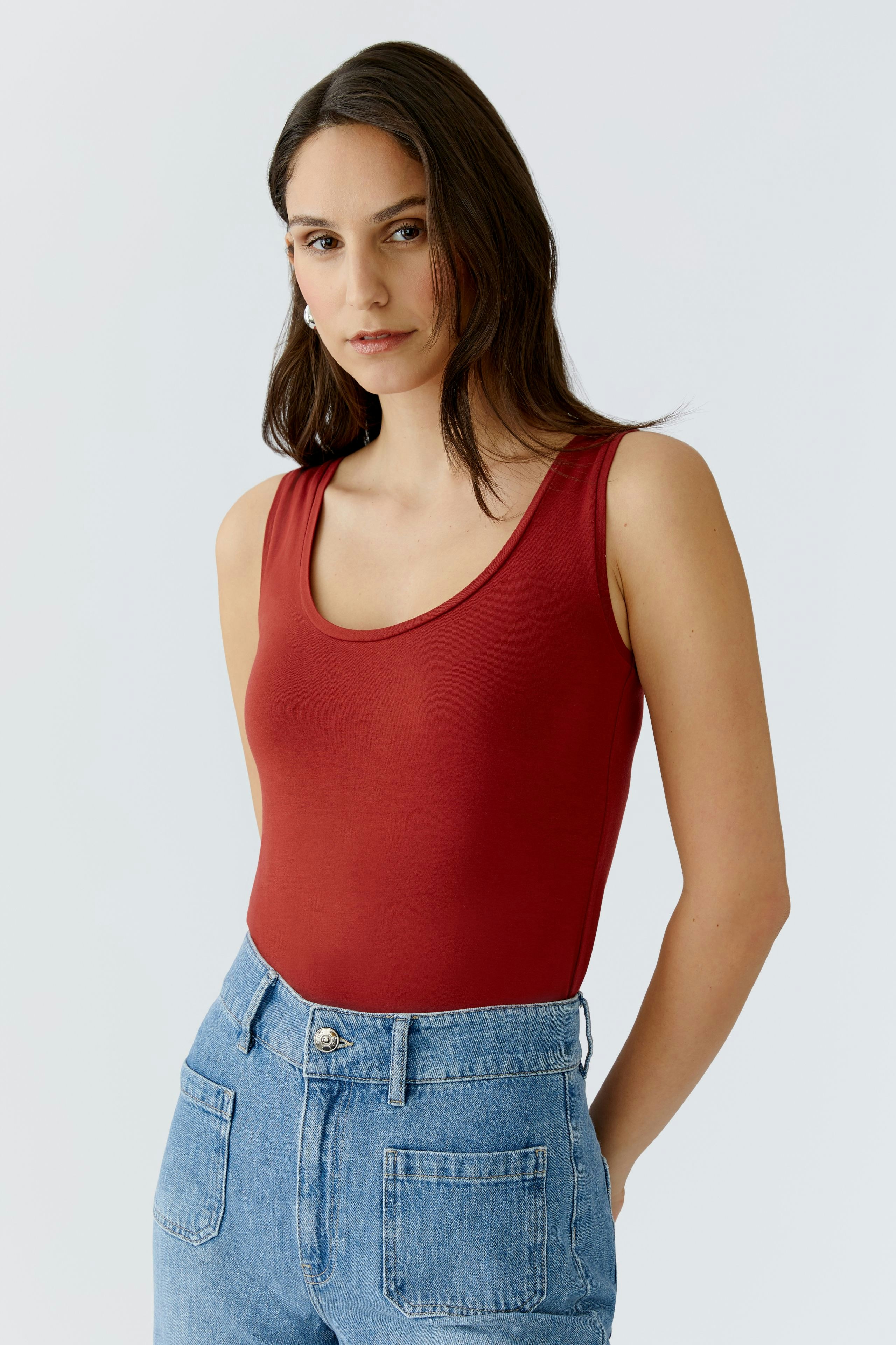 Casual women's tank top: A woman in a red tank top paired with high-waisted jeans, exuding a relaxed vibe.