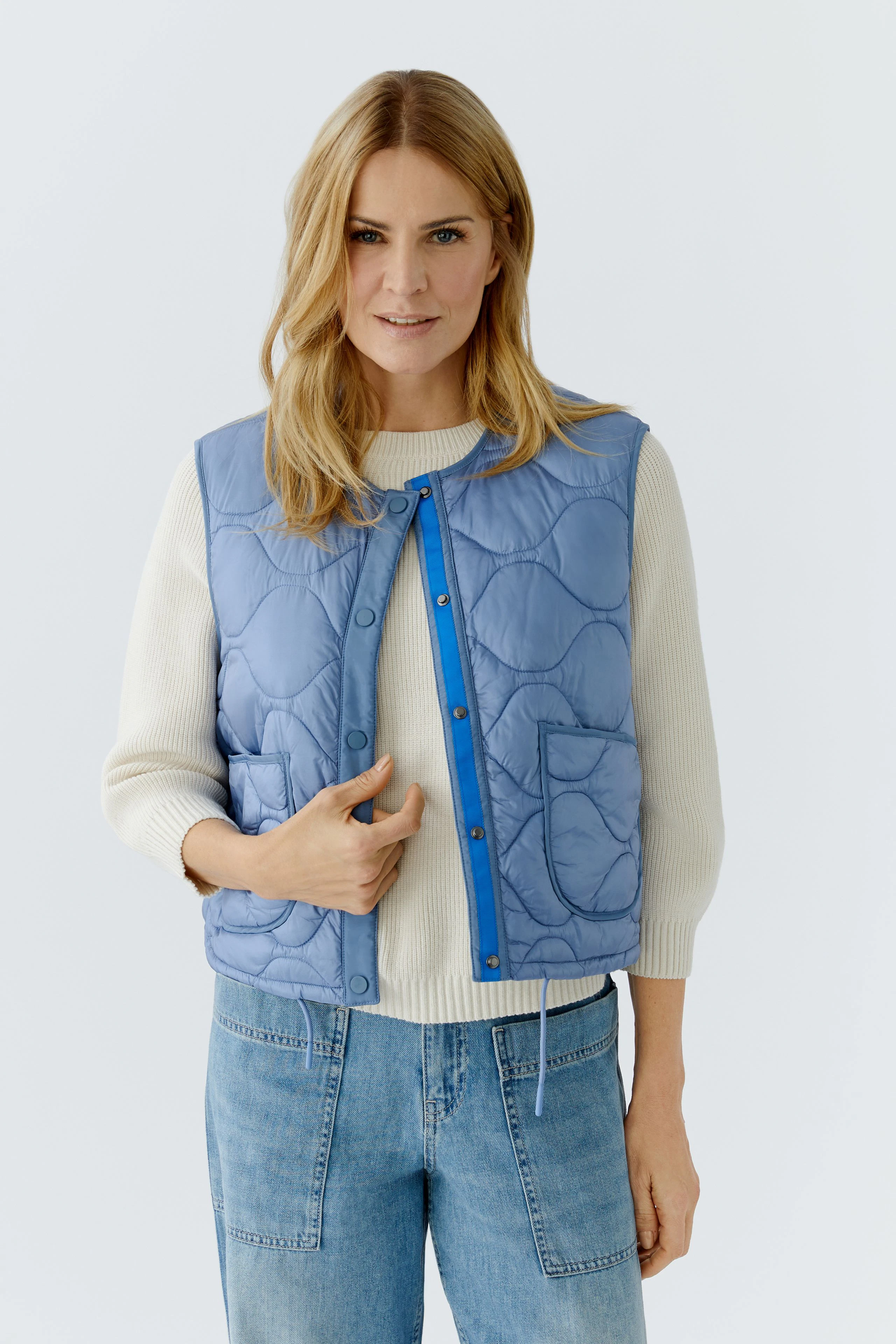 Wendejacke: Frau trägt eine blaue, gesteppte Wendejacke mit praktischen Taschen und lässigem Look.