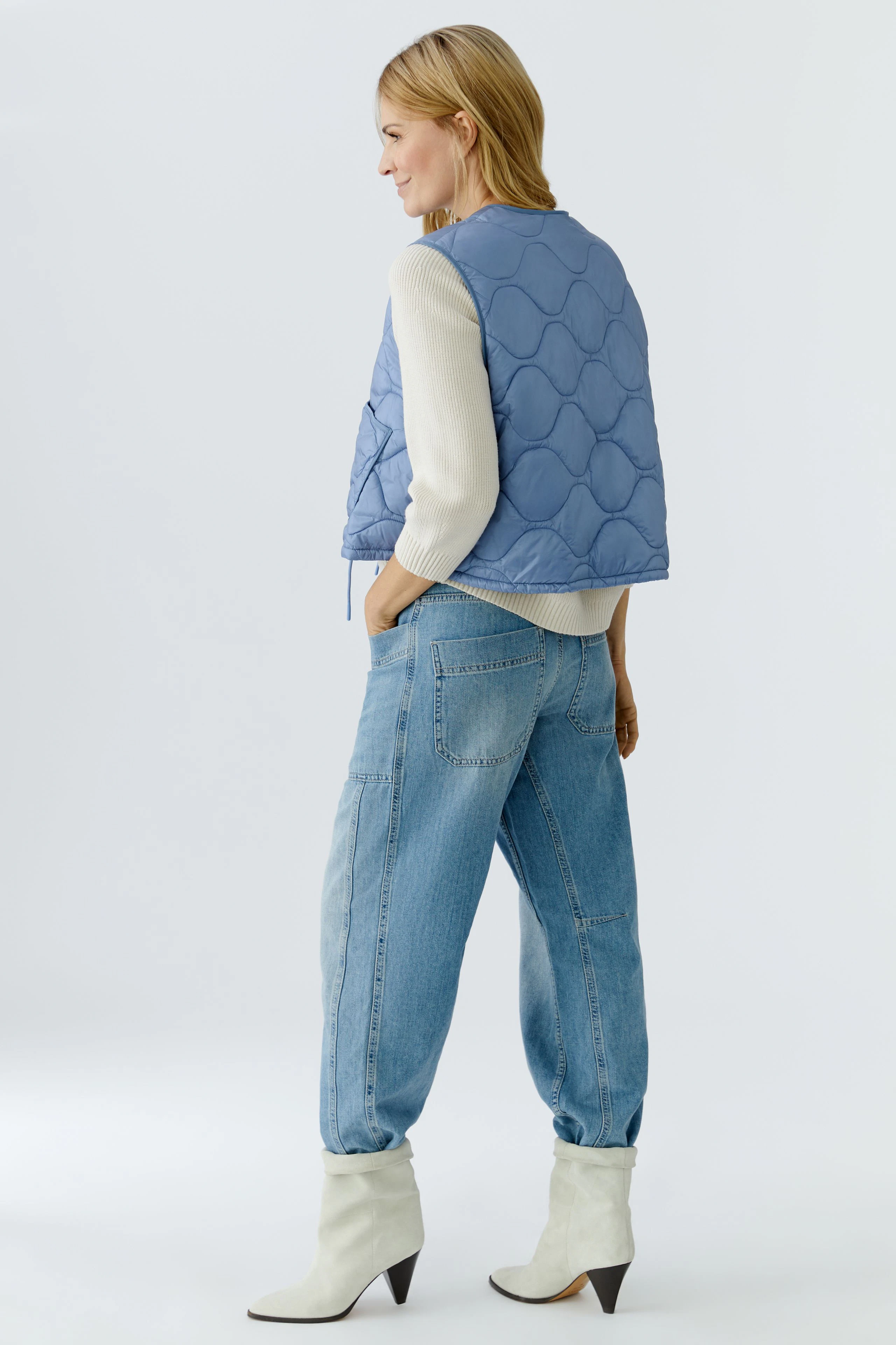 Wendejacke: Frau trägt eine blaue, gesteppte Wendejacke über einem hellen Pullover und lässigen Jeans.