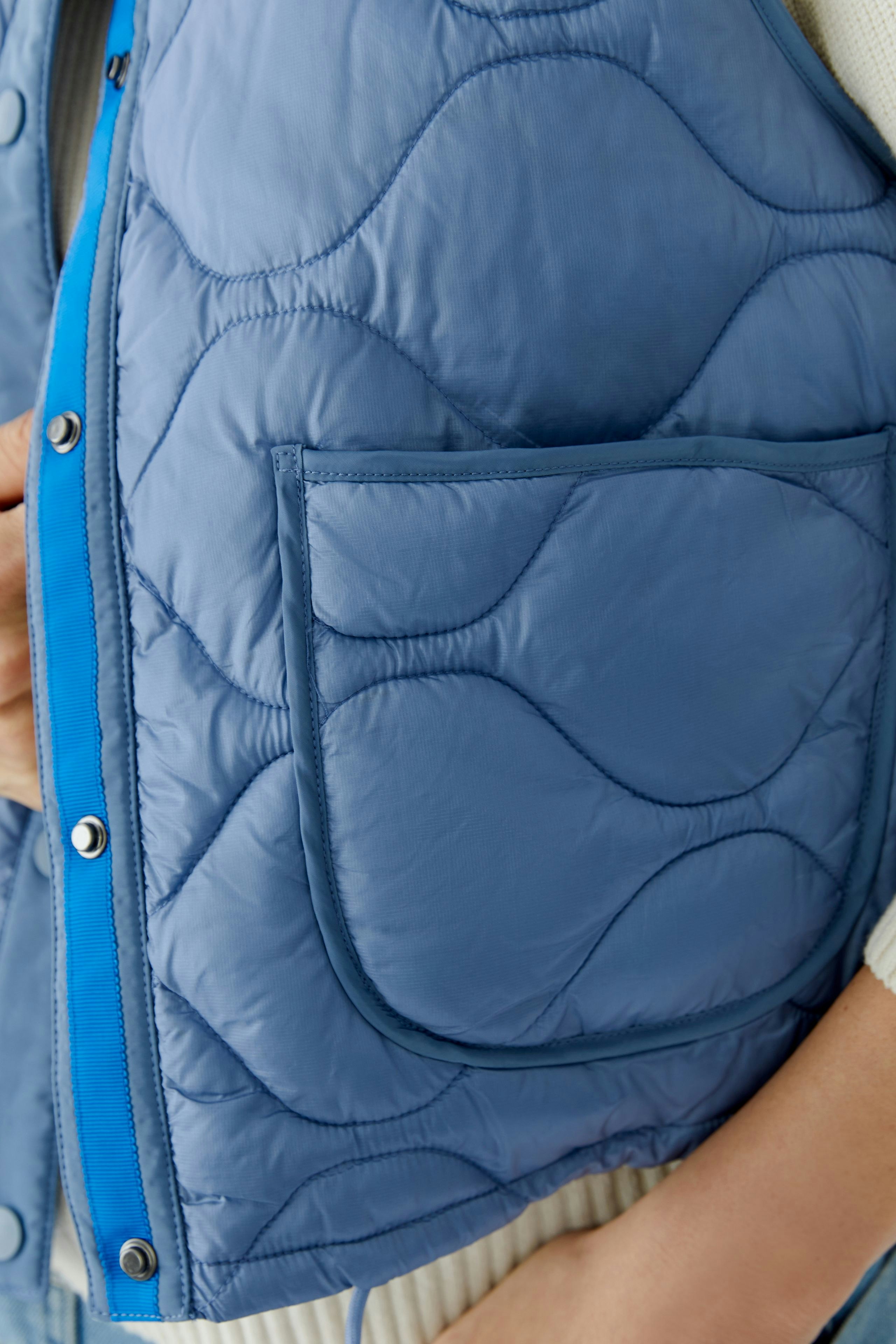 Reversible jacket: Woman in a blue quilted jacket with a pocket, showcasing a casual style.