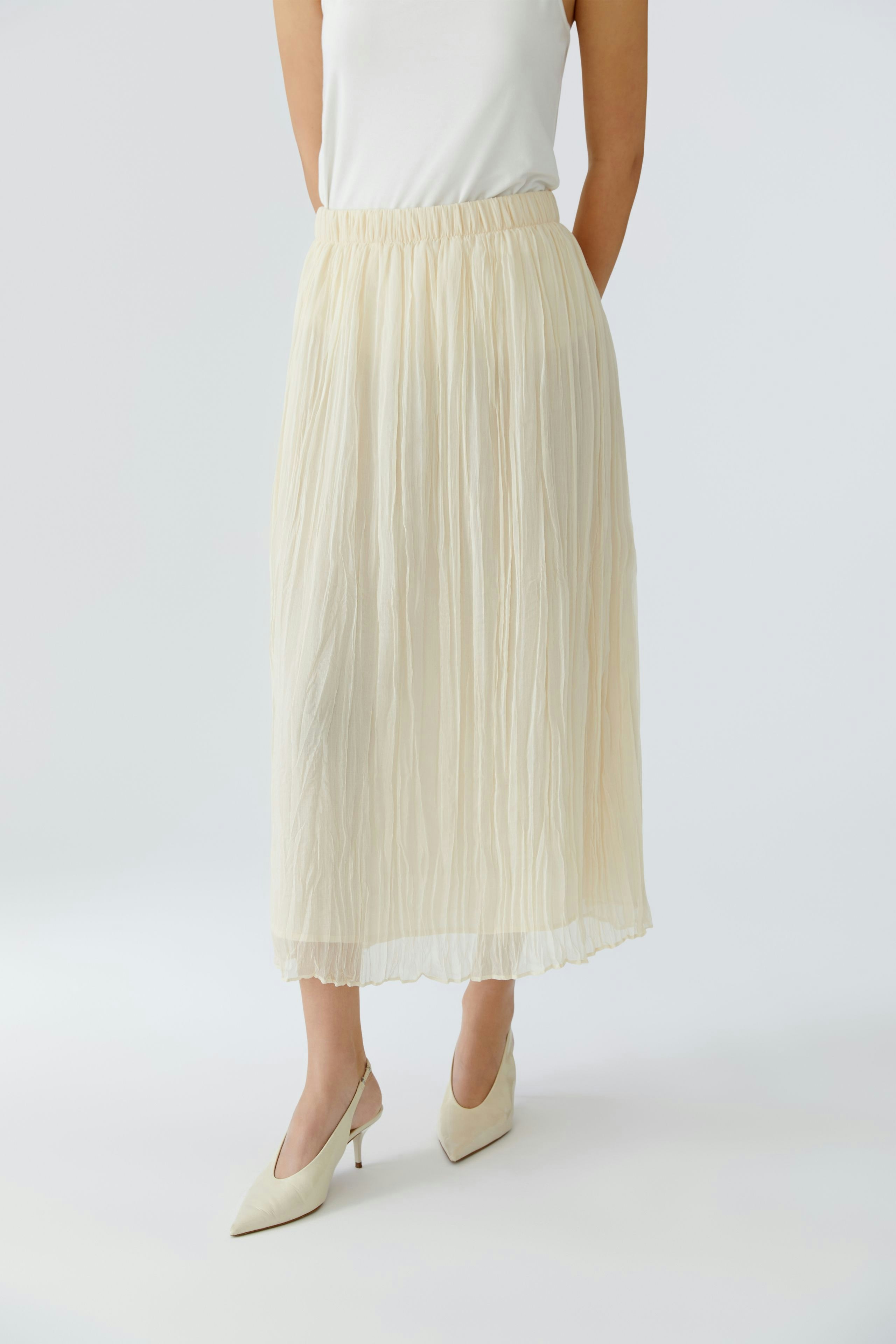 Light pleated skirt: Woman in a flowing cream skirt paired with stylish heels.