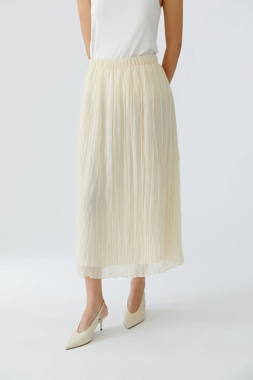 Light pleated skirt: Woman in a flowing cream skirt paired with stylish heels.